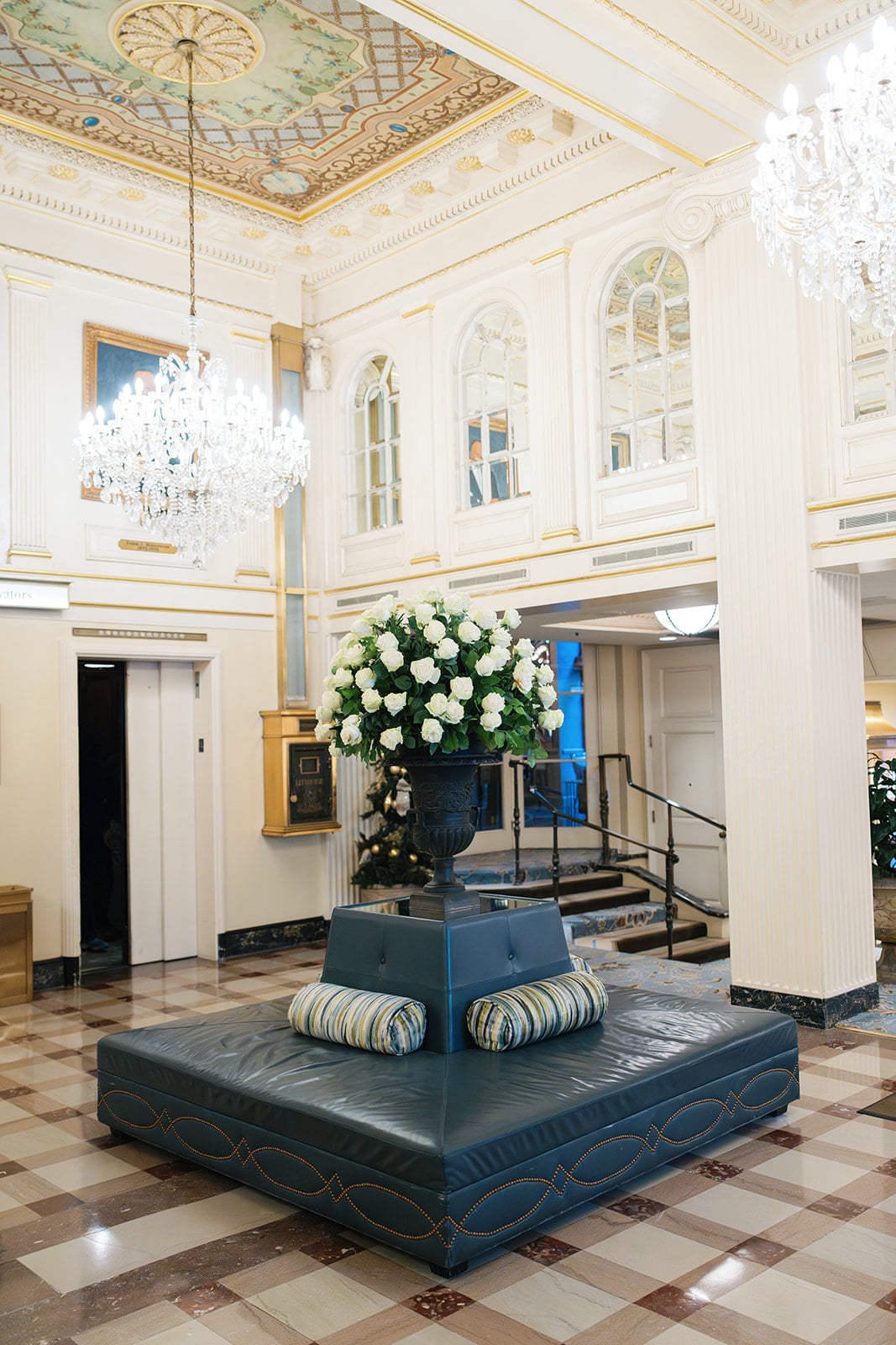 Grand New Orleans hotel lobby with opulent crystal chandeliers, a large urn of white roses, and elegant seating.