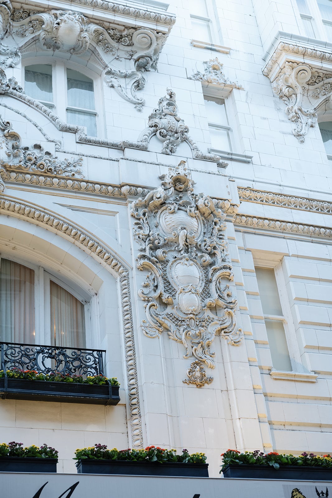 Ornate facade of a historic New Orleans building featuring intricate carvings, a wrought-iron balcony, and flower boxes.