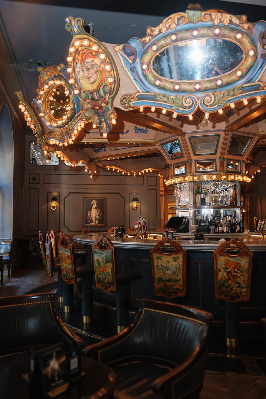 Ornate New Orleans carousel bar featuring a lit, whimsical ceiling and uniquely painted animal bar stools.