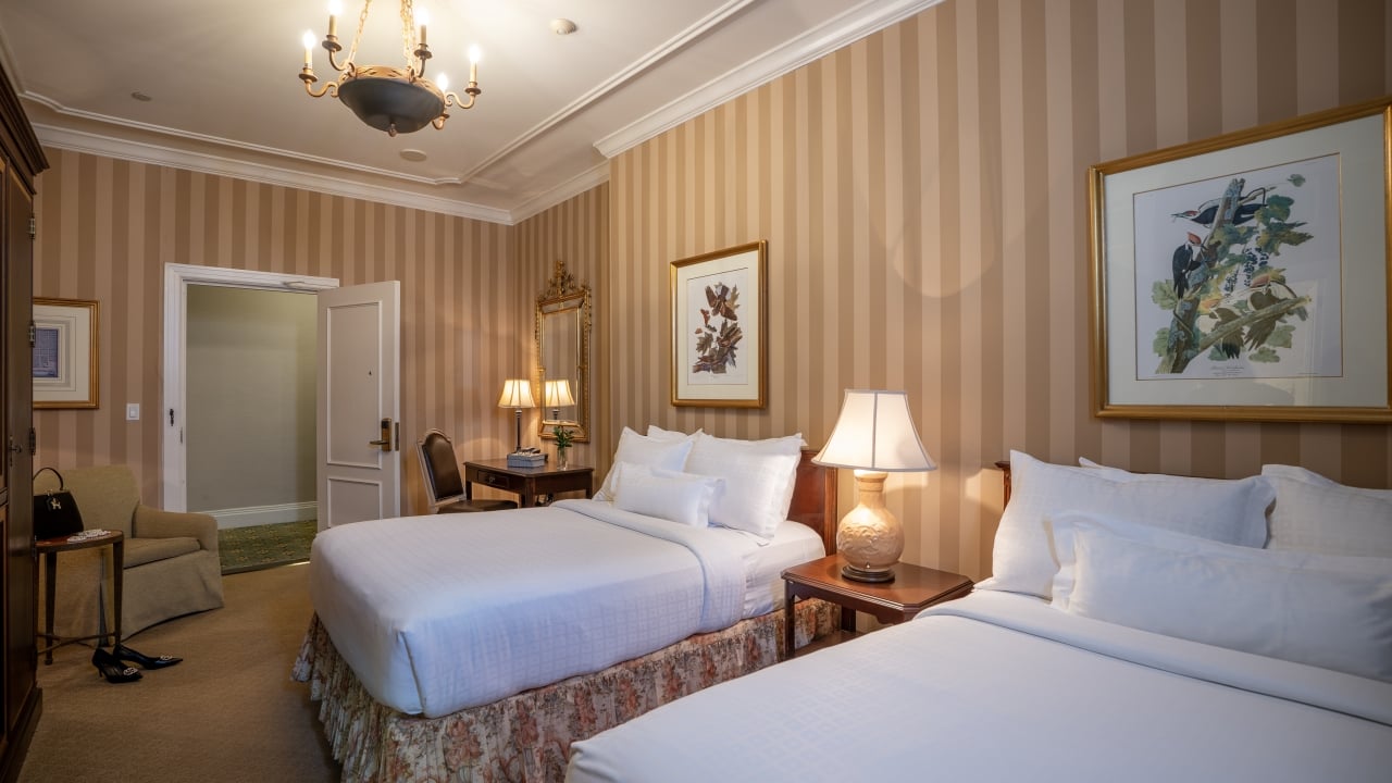 A hotel room with two double beds, striped wallpaper, and a chandelier.