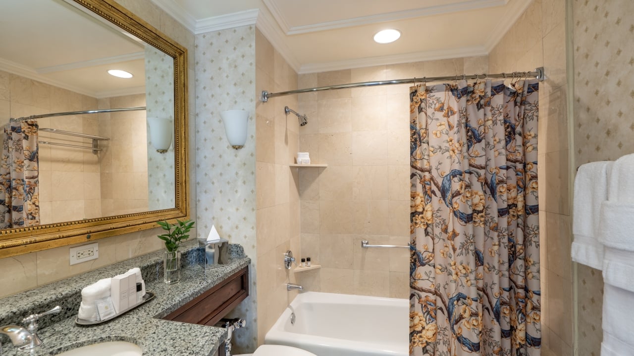 A clean bathroom with a granite countertop, beige tile, a shower curtain, and a bathtub.
