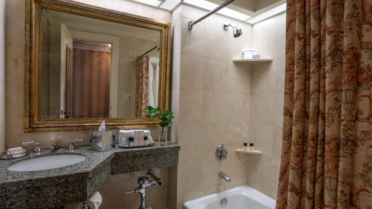 A bathroom with a granite countertop, gold-framed mirror, tiled shower, and bathtub.