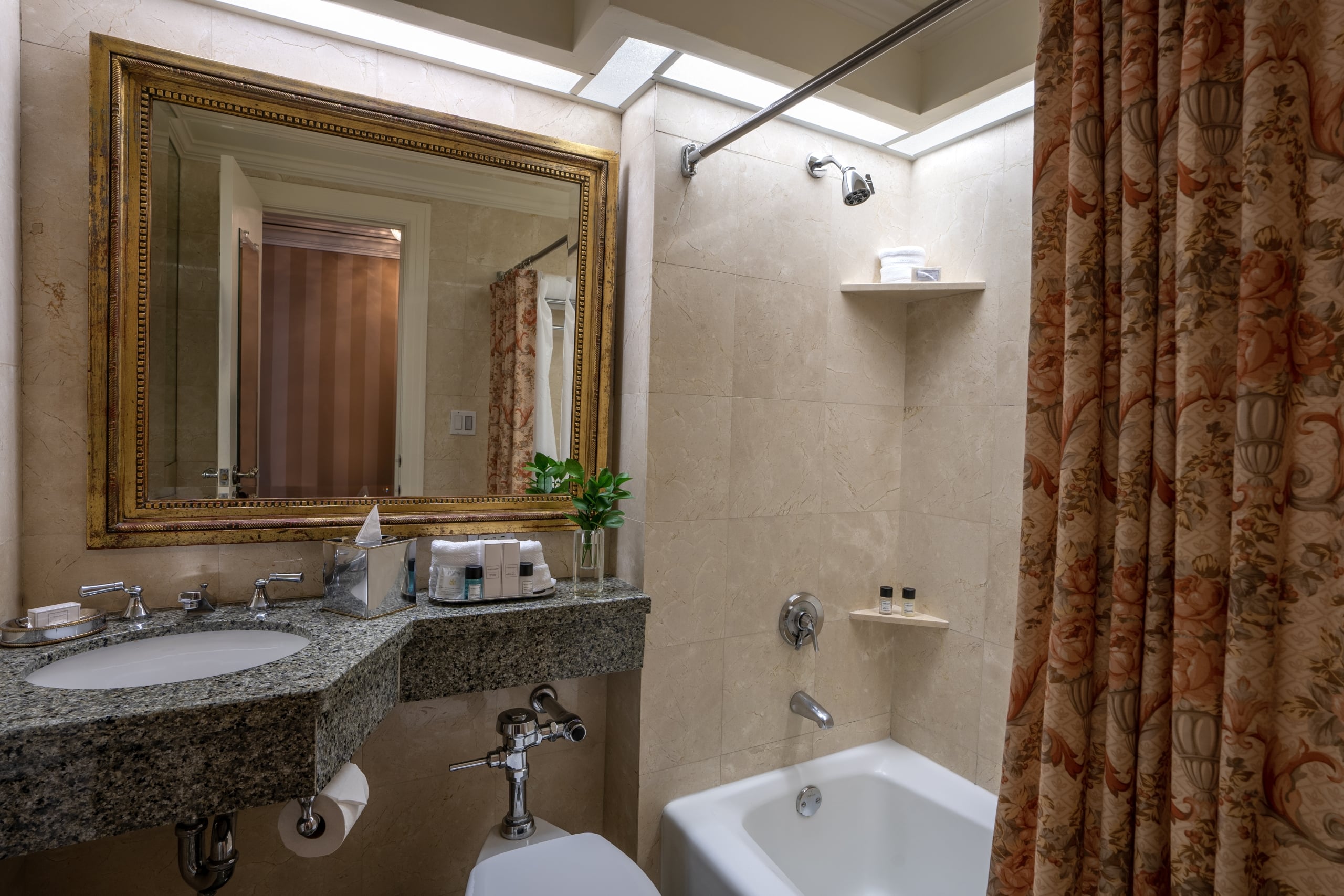 Luxurious hotel bathroom with ornate gold mirror, granite vanity, and a tub with a floral shower curtain.