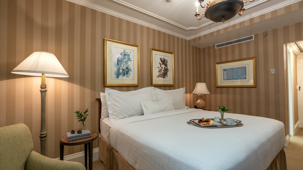 A hotel room with a bed, lamp, artwork, chair, and fruit tray