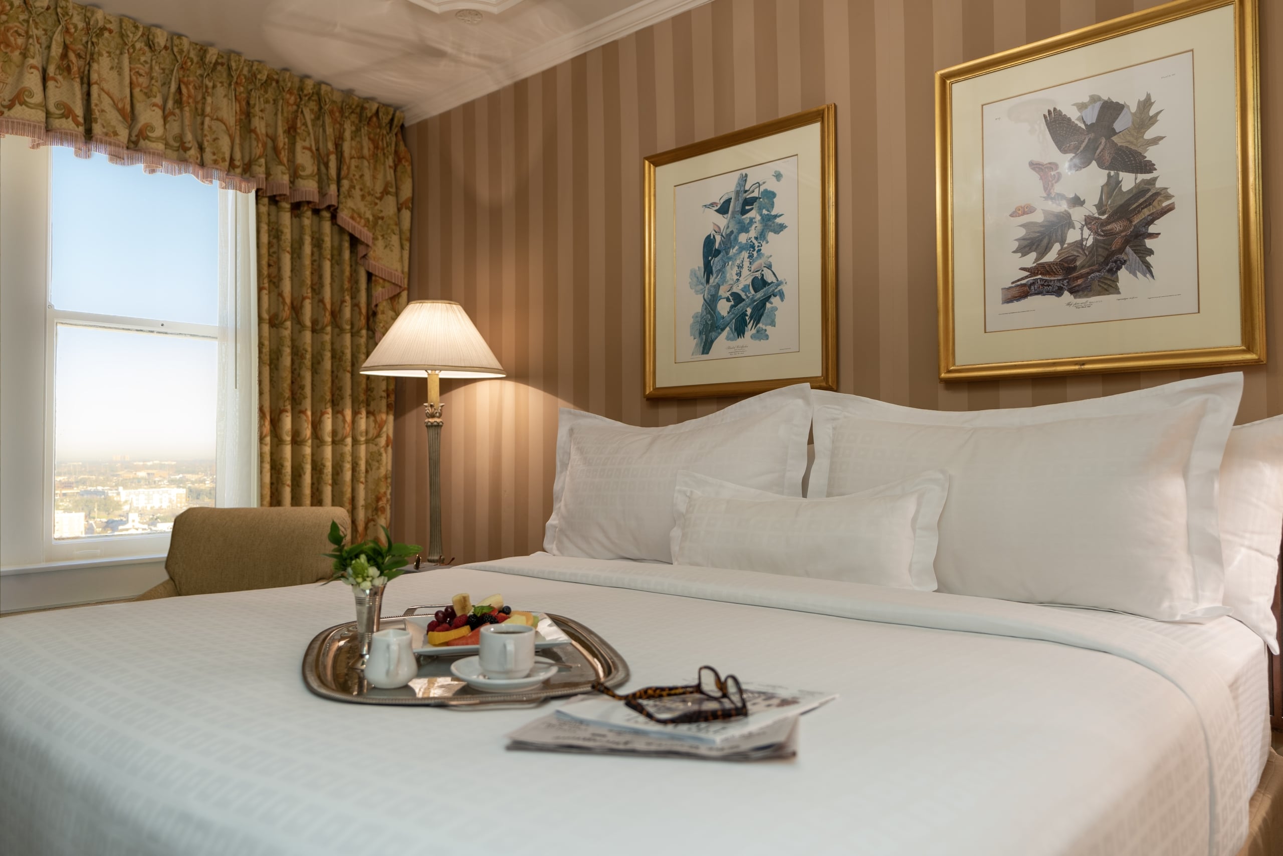 Luxurious New Orleans hotel room: King bed, breakfast tray, city view, and classic bird art.