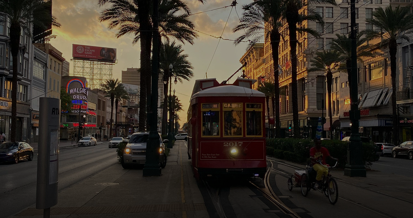 Iconic red New Orleans streetcar on a city street lined with palm trees at sunset. https://www.hotelmonteleone.com/content/uploads/2026/02/1440-hero.png