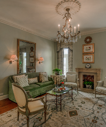 Luxurious living room with green velvet sofa, crystal chandelier, and ornate fireplace in New Orleans.