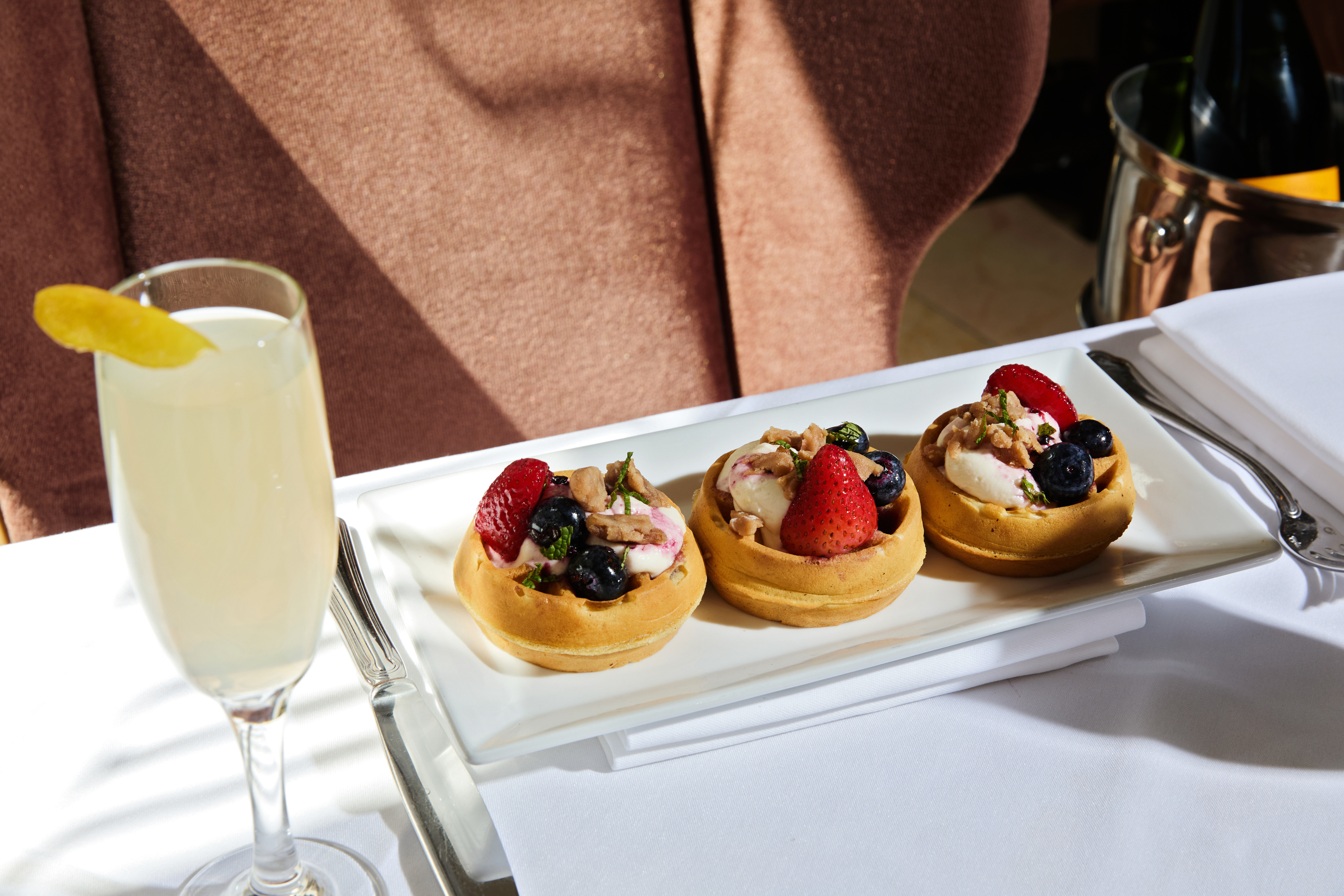 a plate of waffles with fruit and cream and a glass of drink