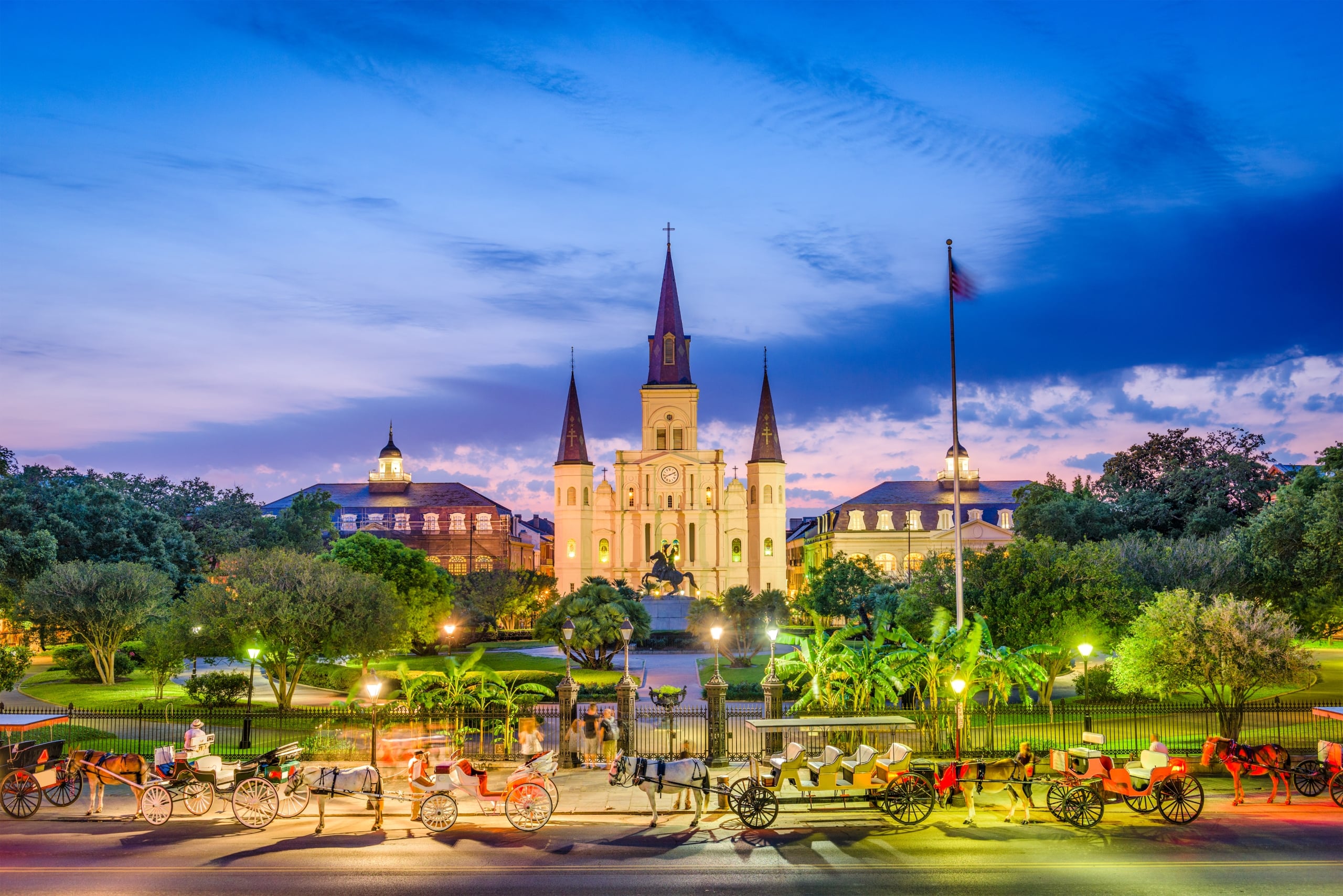 Sunset illuminates St. Louis Cathedral and Jackson Square, New Orleans, with horse carriages.