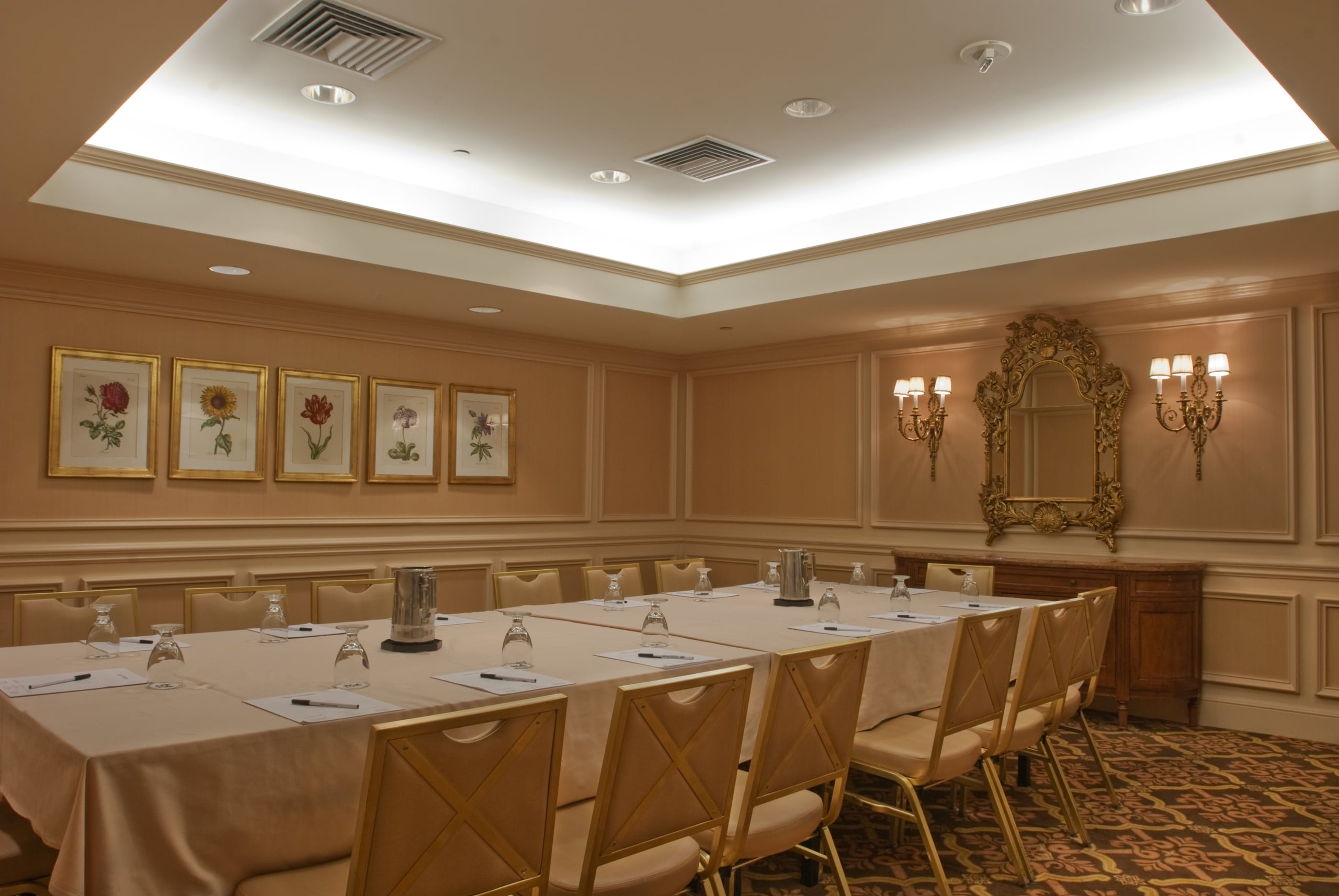 Elegant conference room in a New Orleans hotel with a long table, chairs, botanical art, and ornate mirror.