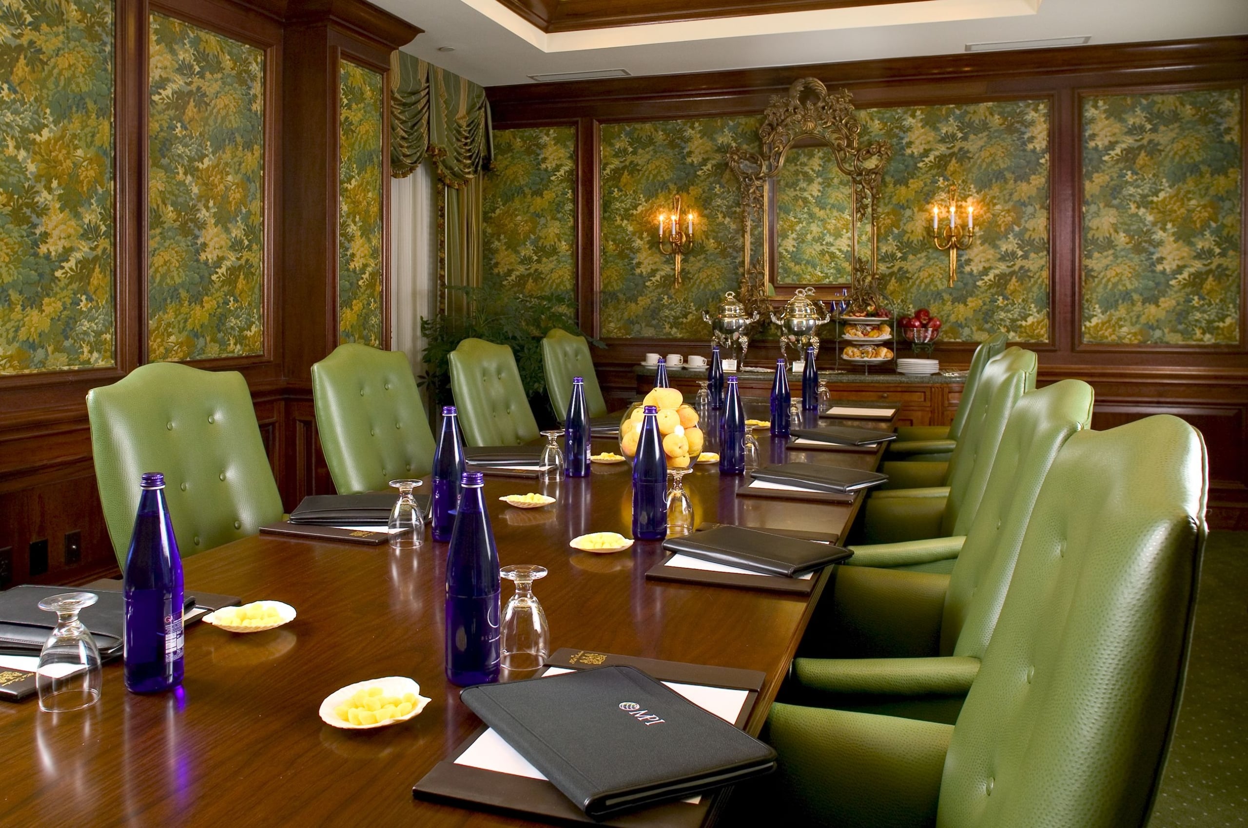 Elegant New Orleans conference room with green chairs, a long table, ornate decor, and refreshments.