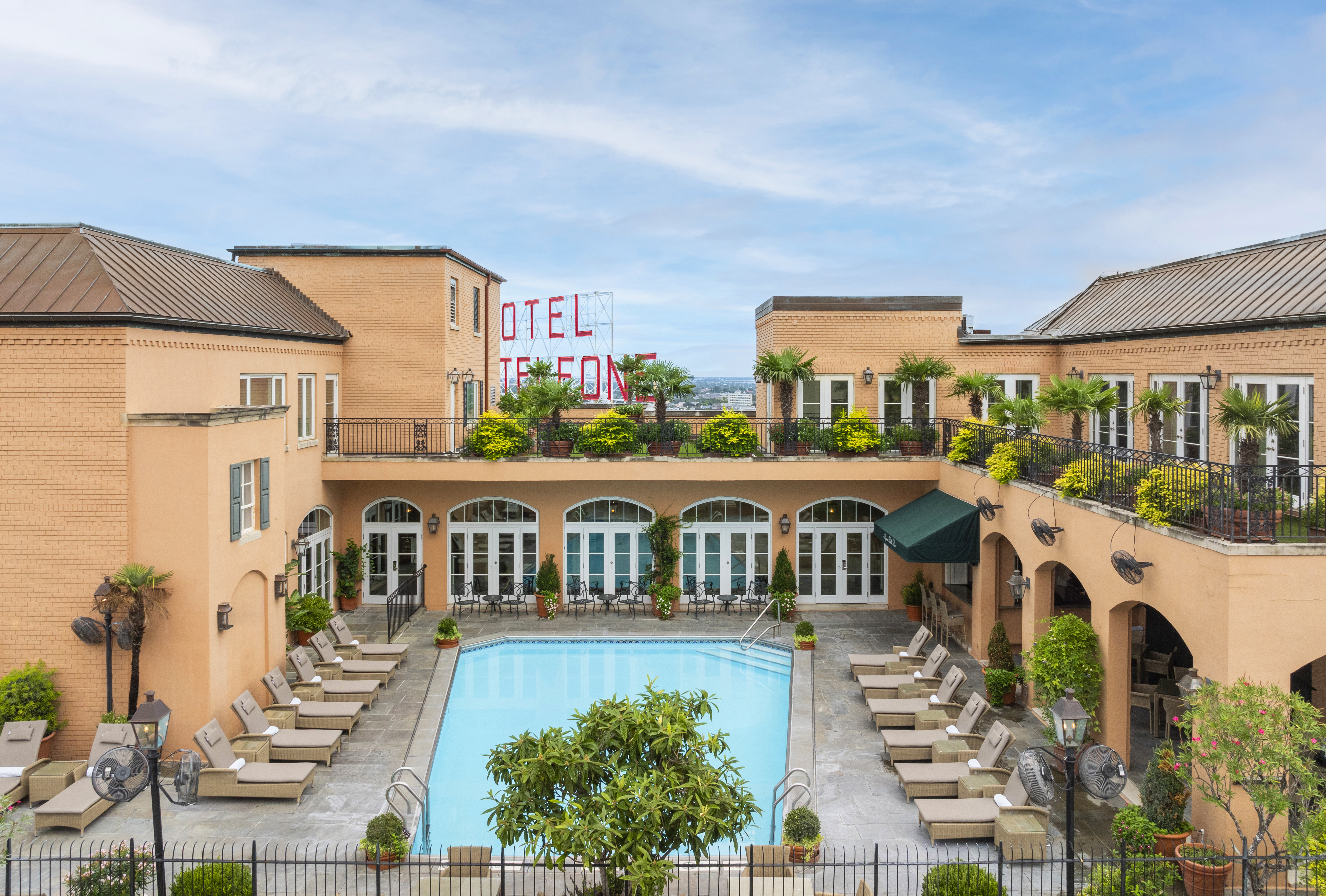 A beige hotel building with a pool and lounge chairs in front of it.