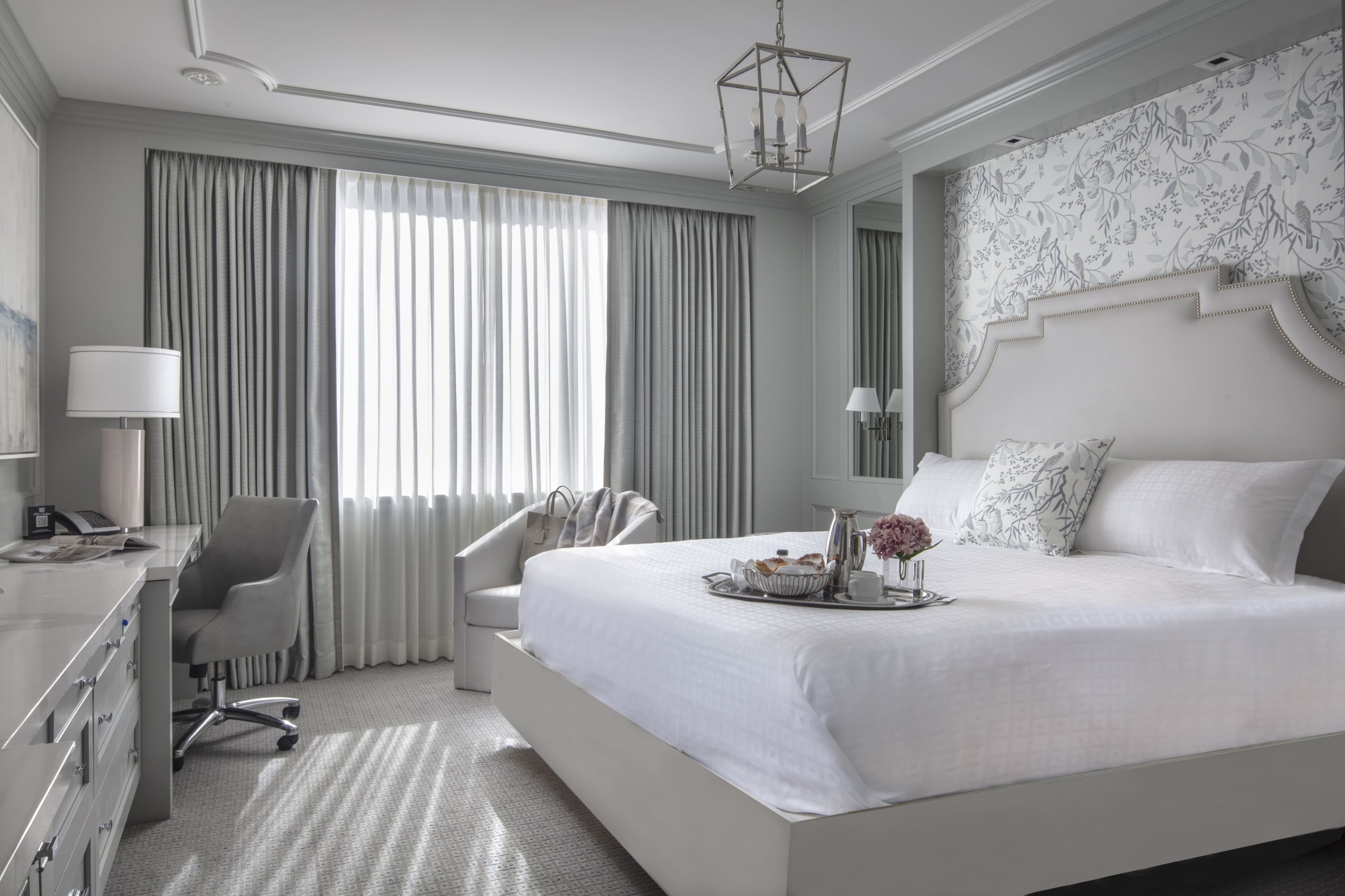 Chic New Orleans hotel room with a plush king bed, breakfast in bed, and elegant avian wallpaper.