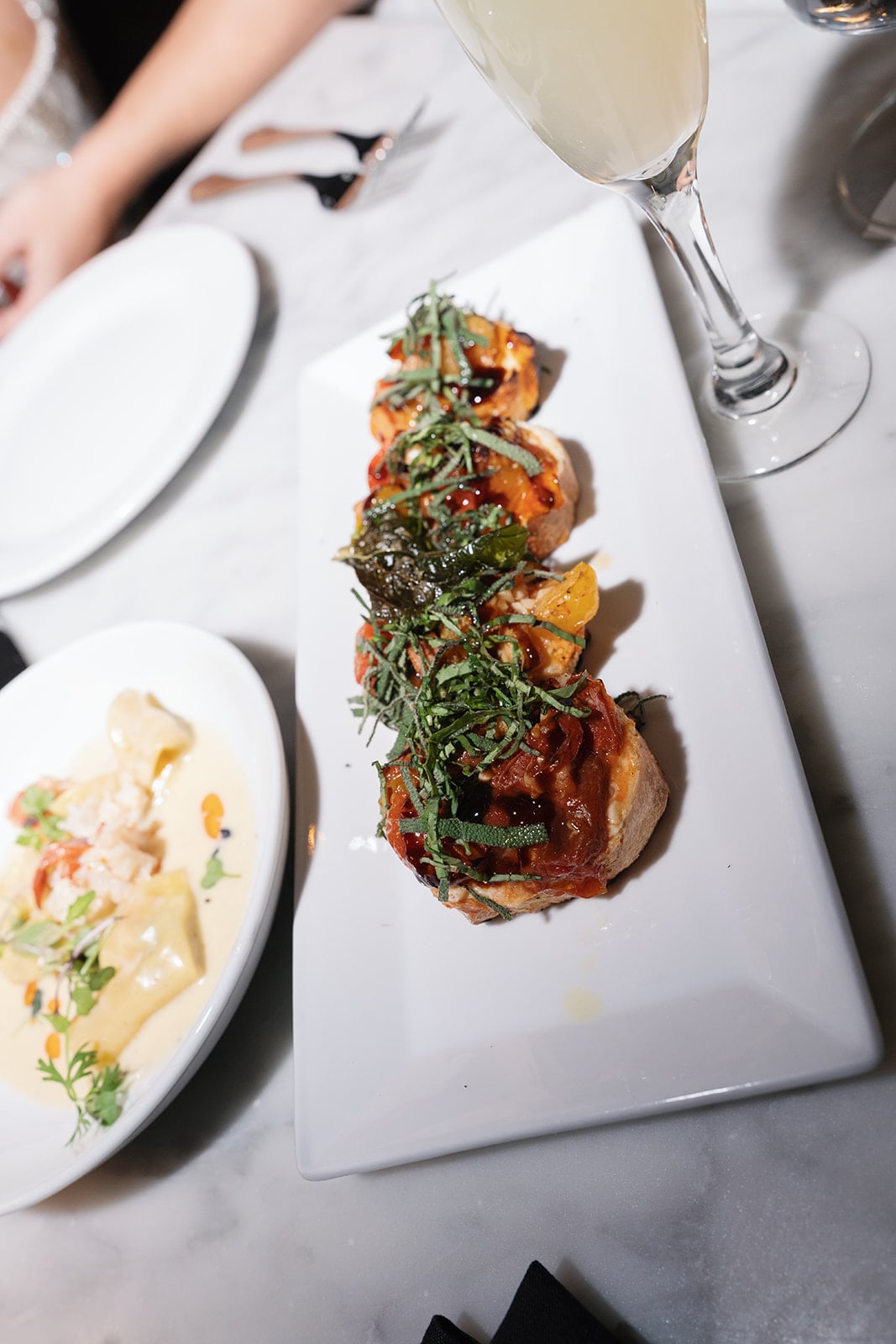 Bruschetta appetizers, creamy pasta, and a cocktail in an elegant New Orleans restaurant setting.