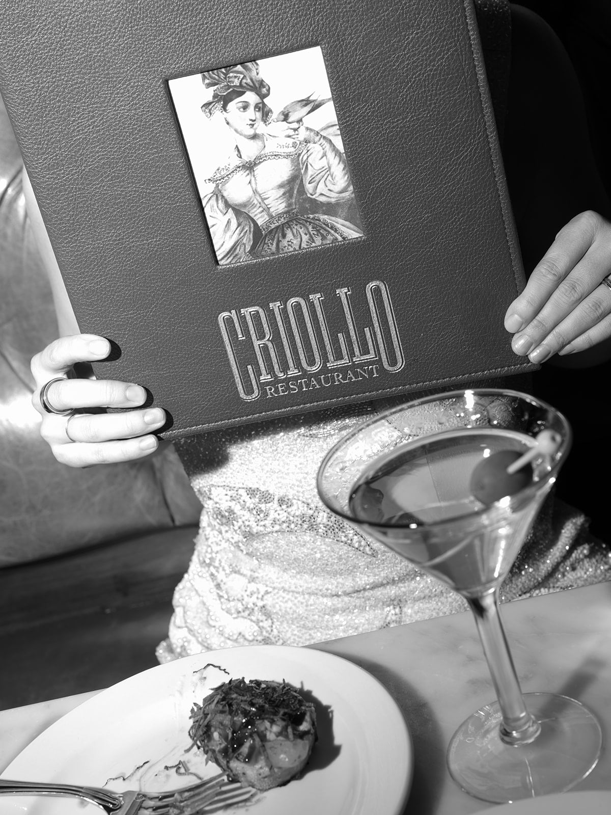 Dining at Criollo Restaurant: a menu held by a guest, a martini, and an appetizer in New Orleans.