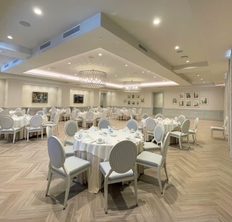A large, well-lit banquet room with round tables set for a meal.