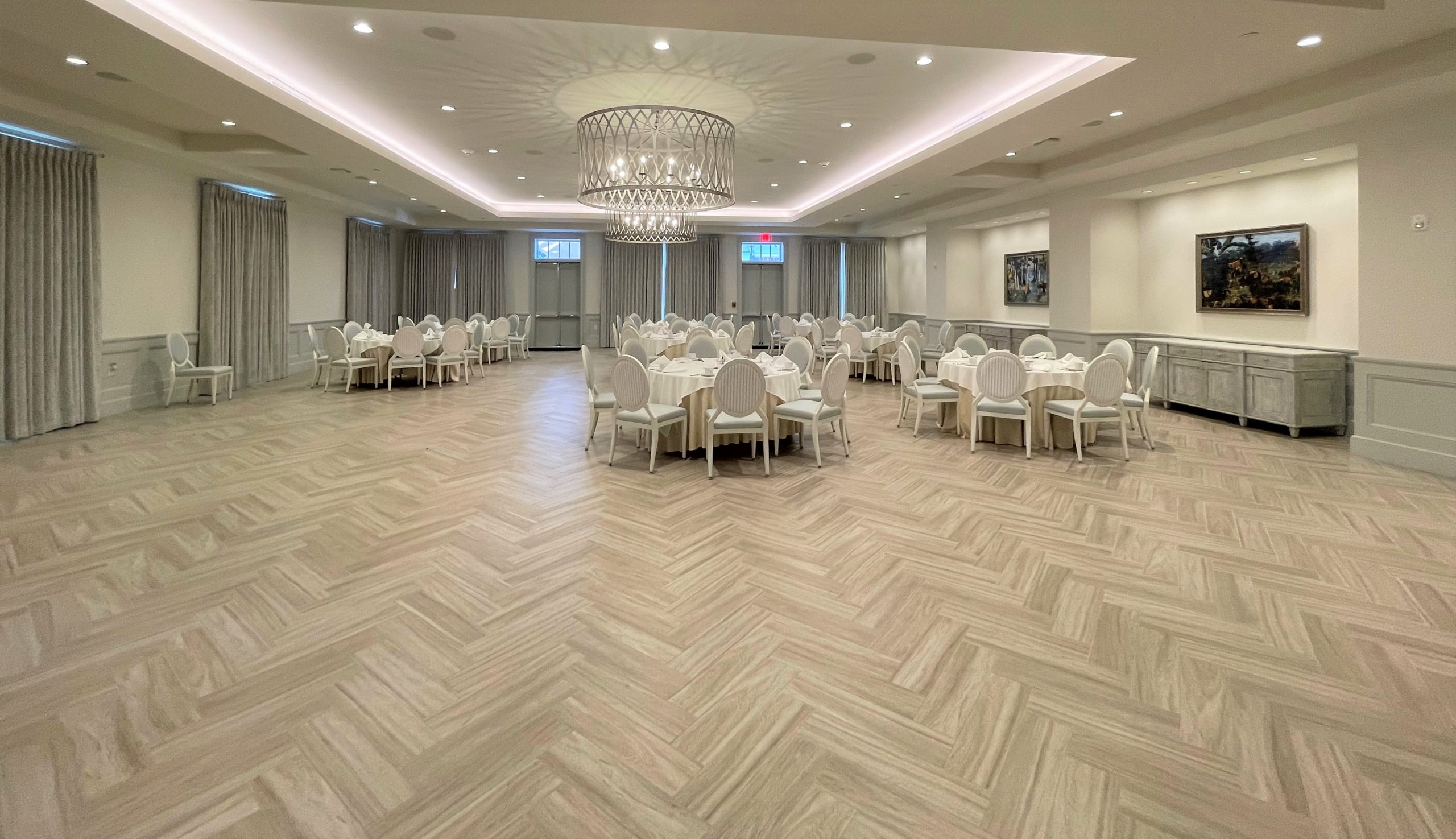 Elegant ballroom with light herringbone floor, round tables, white chairs, and ornate chandeliers in New Orleans.