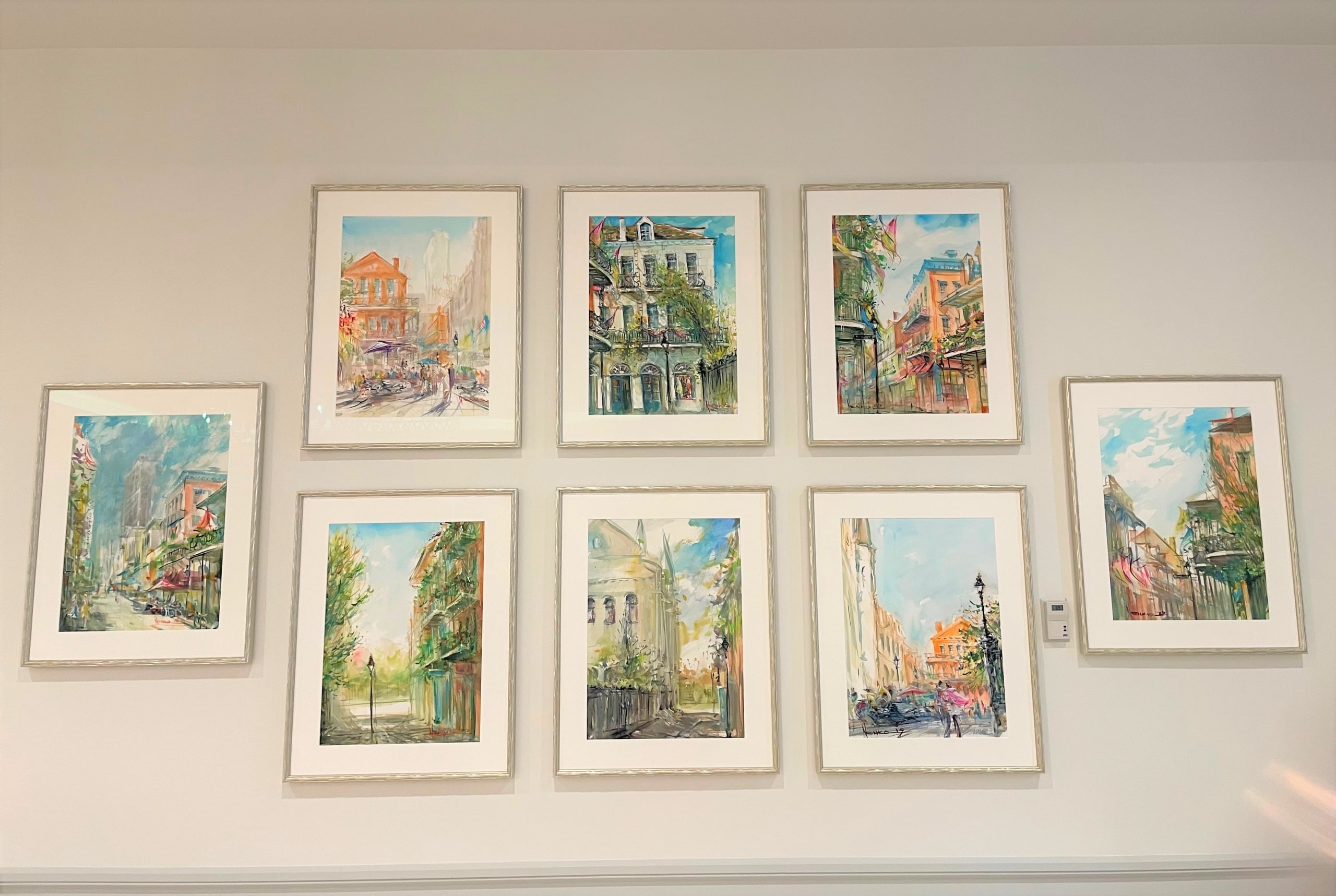 Eight framed watercolor paintings of vibrant New Orleans street scenes and architecture.