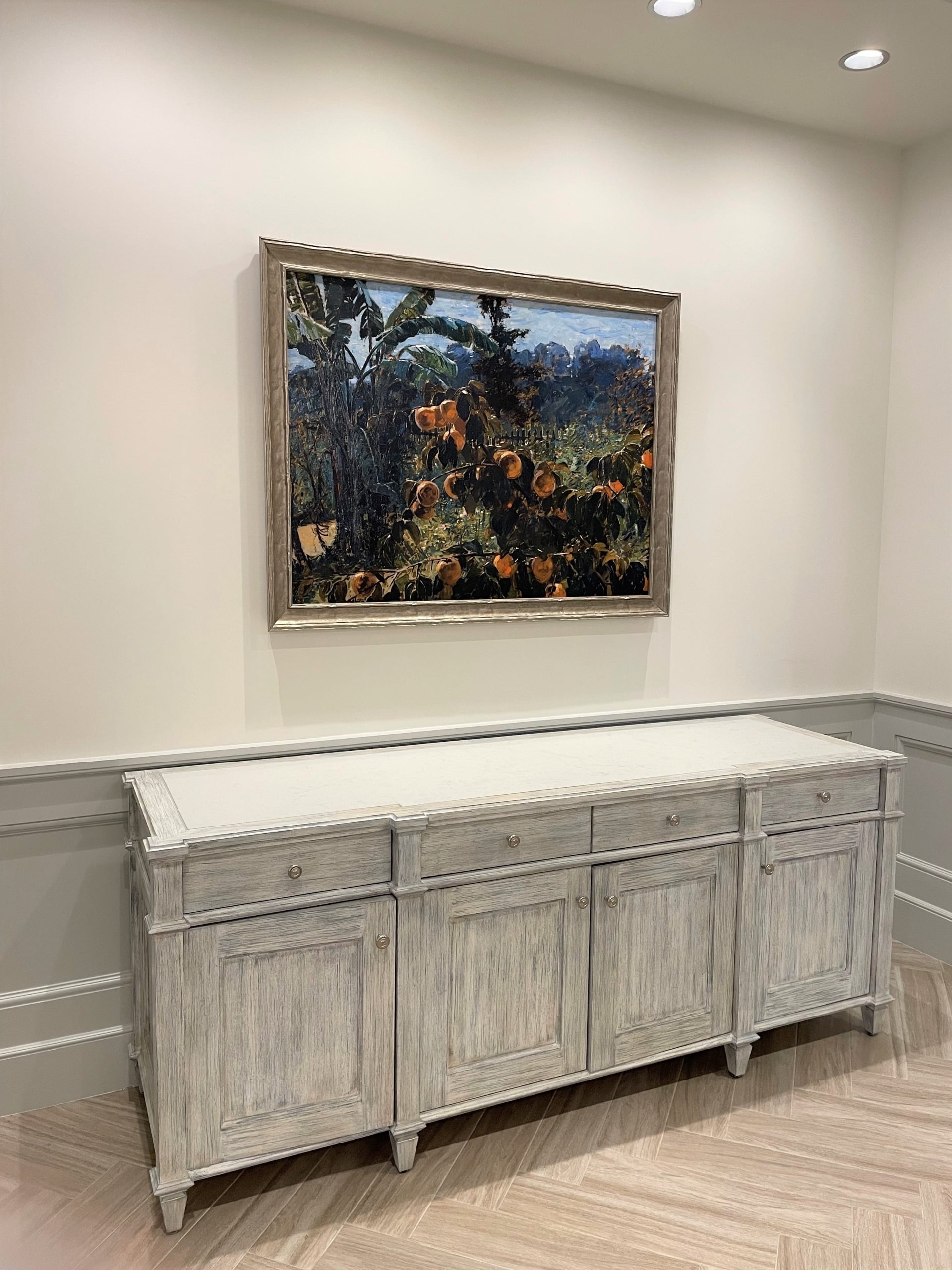 Chic distressed wood console with a framed New Orleans tropical landscape painting, in a welcoming interior.