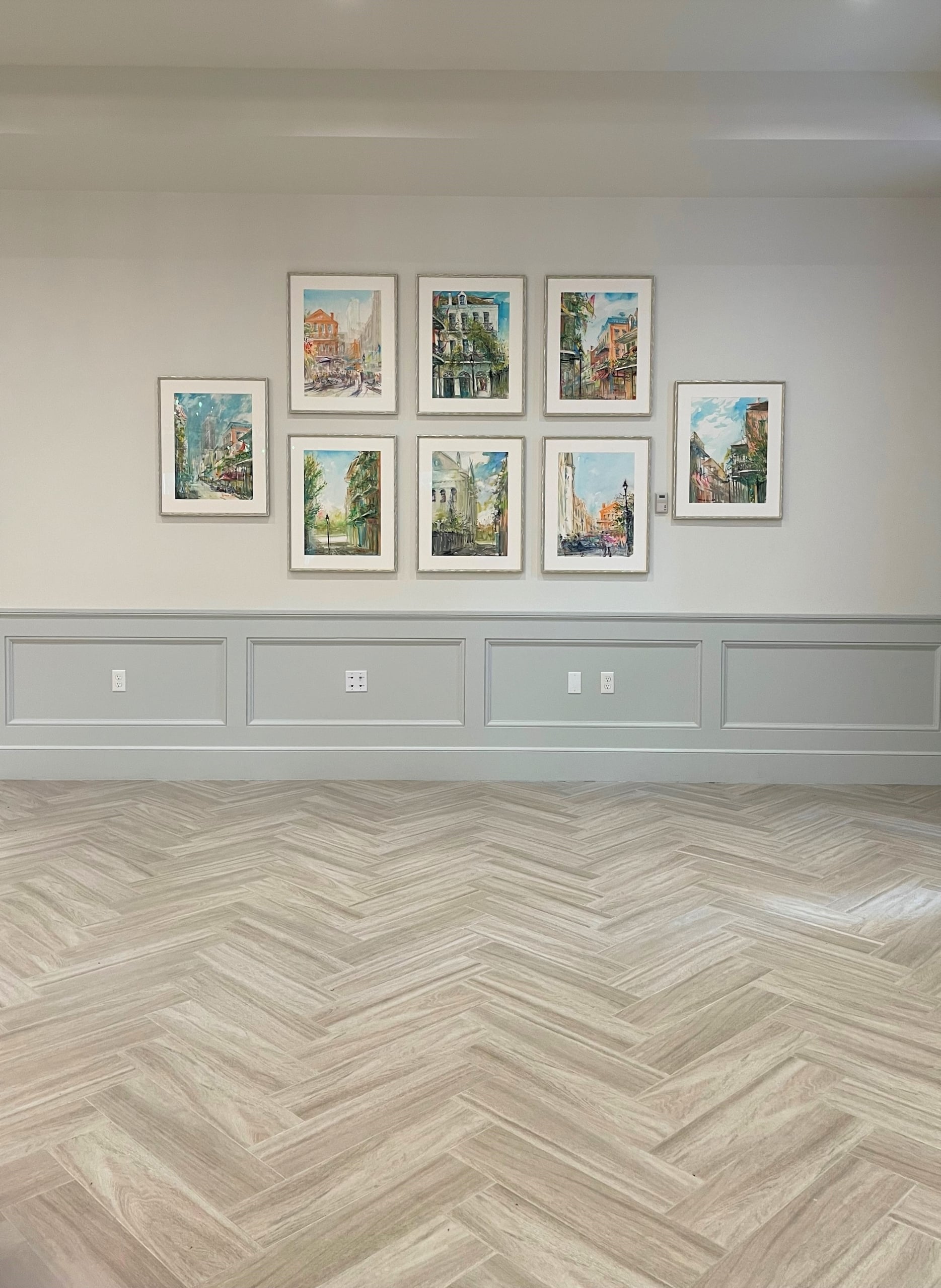 Elegant room with herringbone floors and a gallery of eight vibrant watercolor paintings of New Orleans street scenes.
