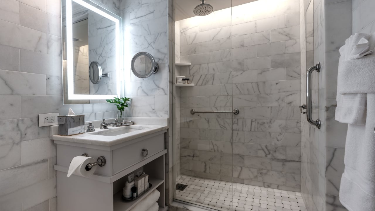 A clean bathroom with marble tiles, a glass shower door, and a sink with a mirror above it.