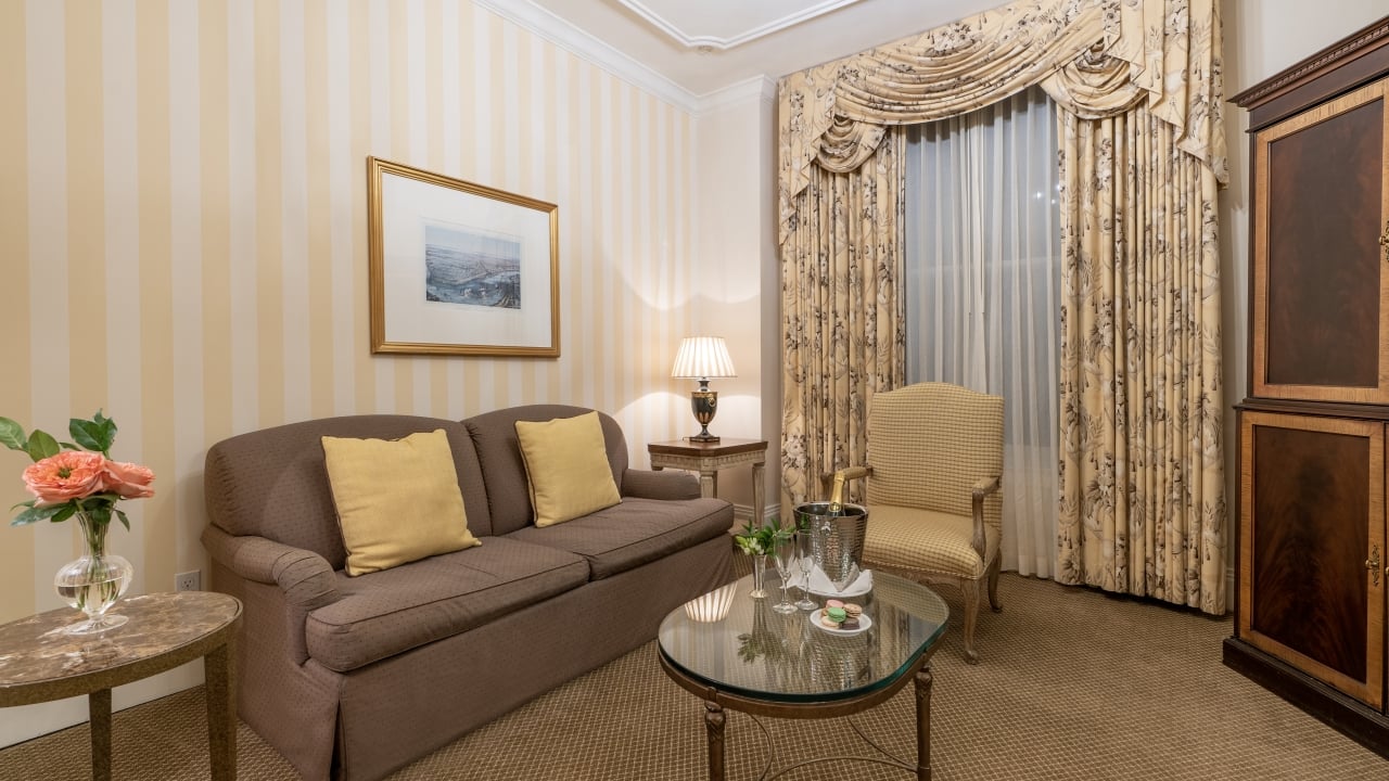 A wide view of a hotel room with a sofa, coffee table, armchair, and end table.