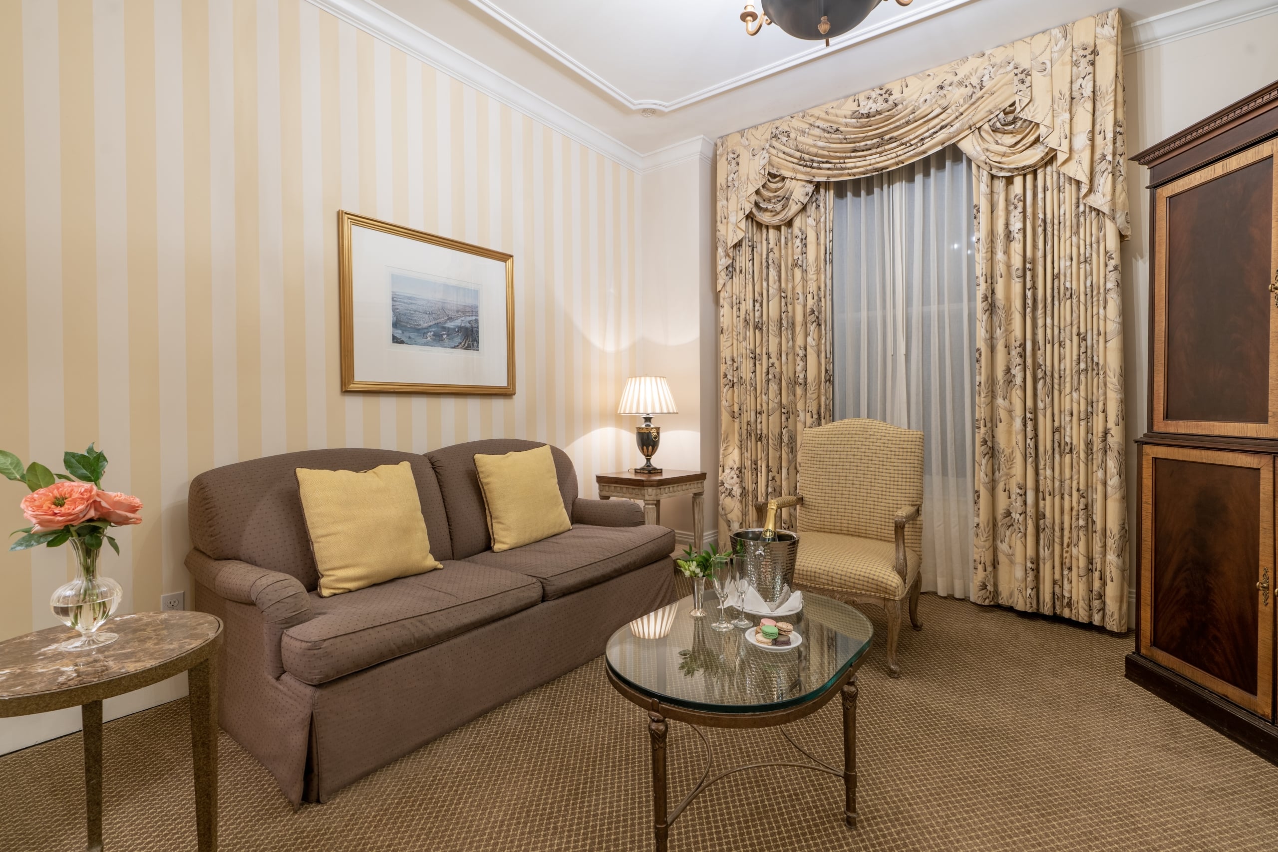 Elegant New Orleans hotel suite living room with a brown sofa, patterned drapes, and welcome treats.