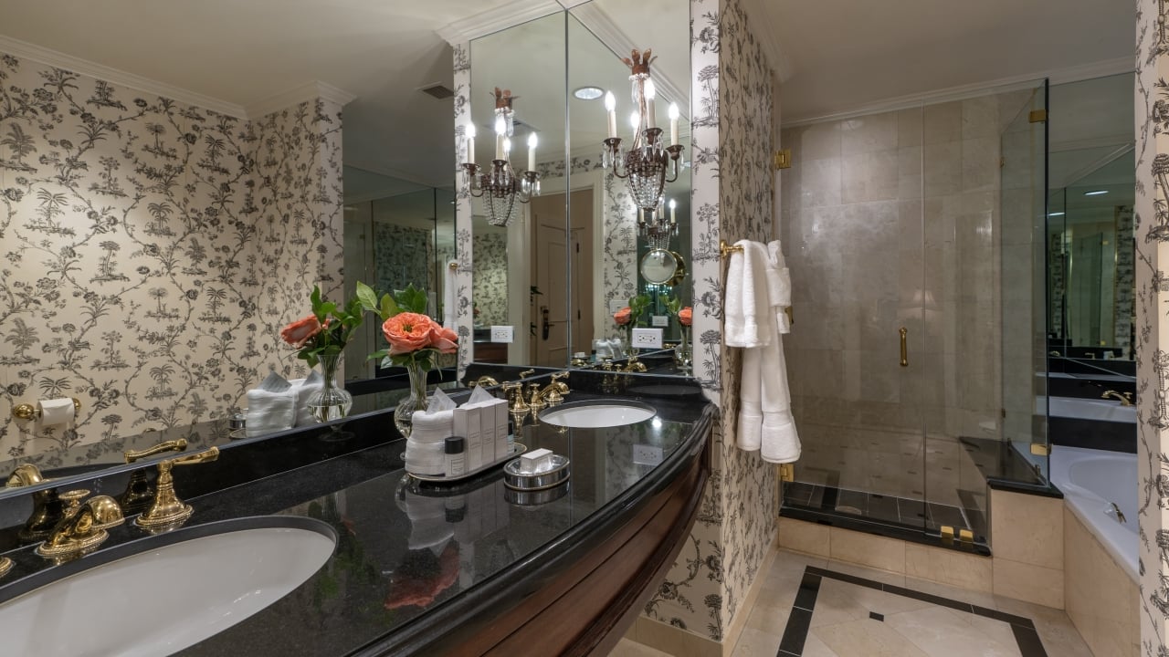 A luxurious bathroom with a double vanity, floral wallpaper, and a large walk-in shower.