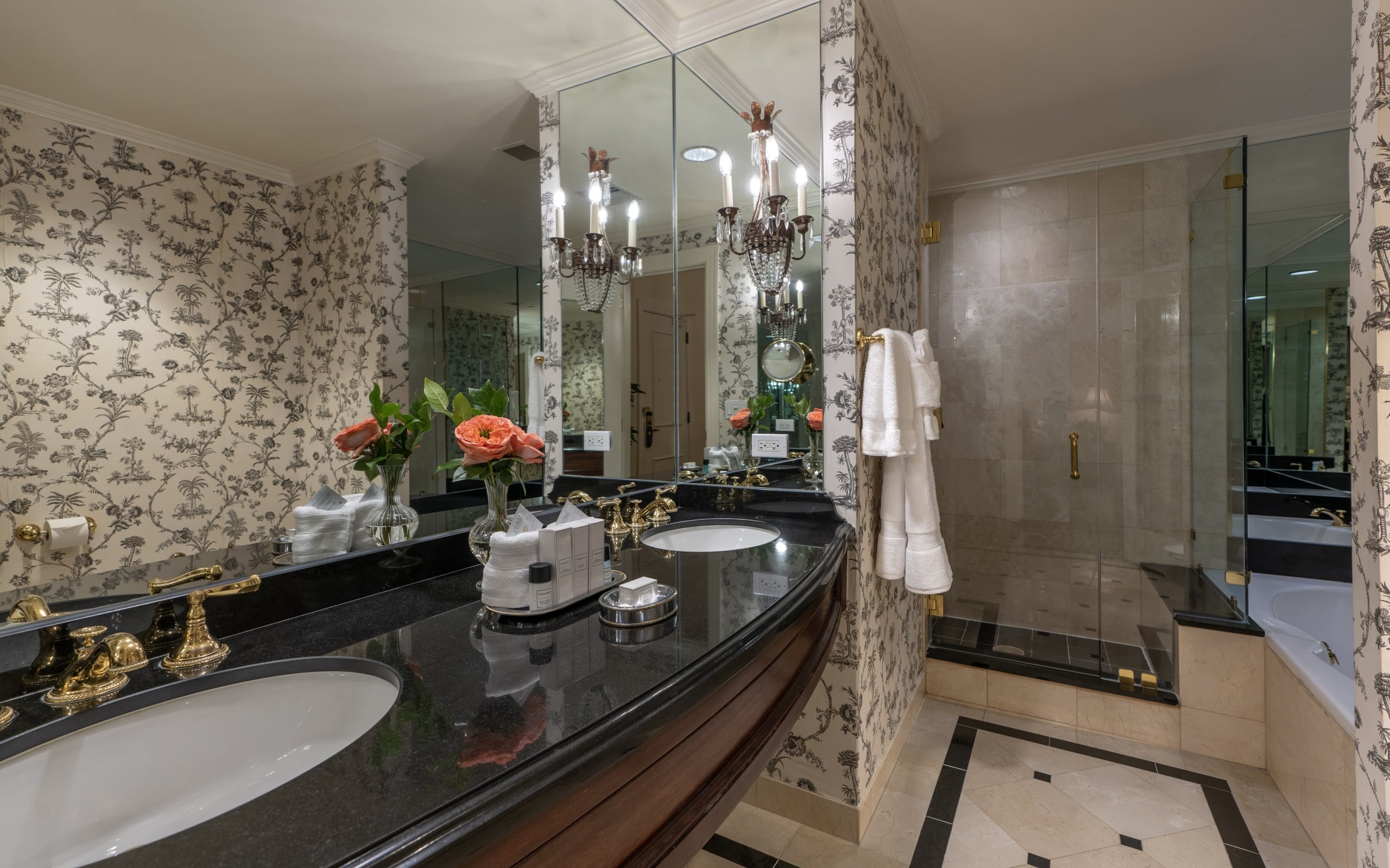 Elegant New Orleans hotel bathroom with double vanity, fresh flowers, scenic wallpaper, and shower.