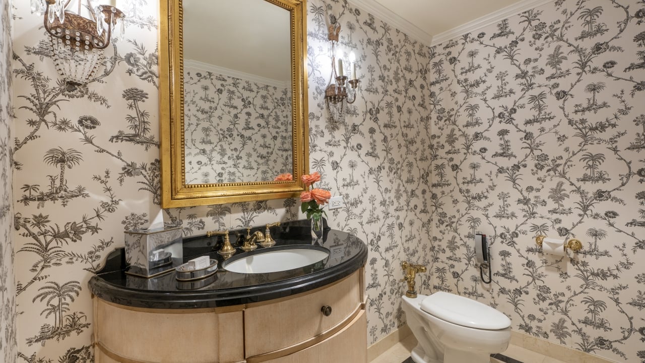 A bathroom with a black granite countertop, gold fixtures, and floral wallpaper