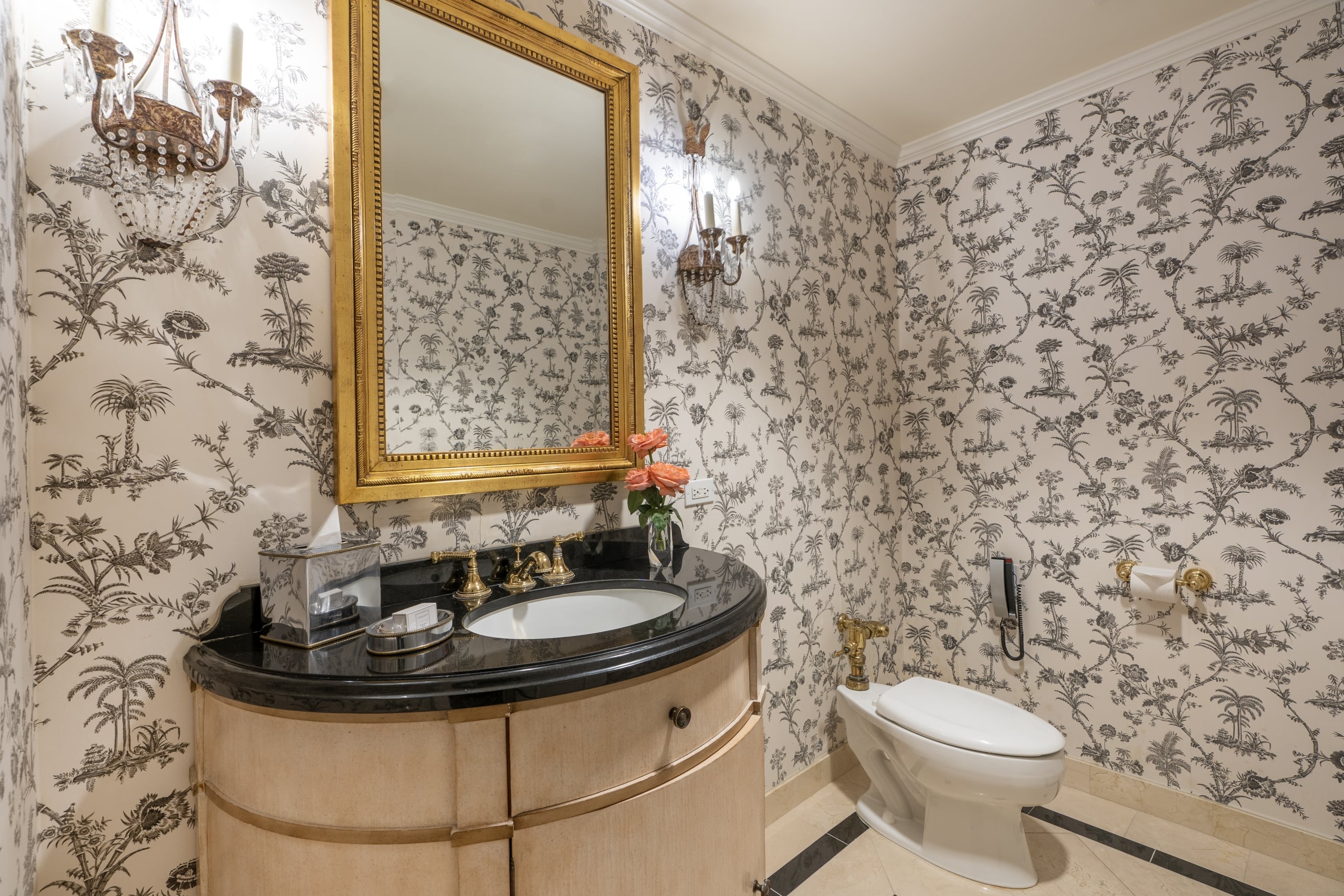 Elegant New Orleans style bathroom with botanical wallpaper, ornate gold mirror, and marble vanity.