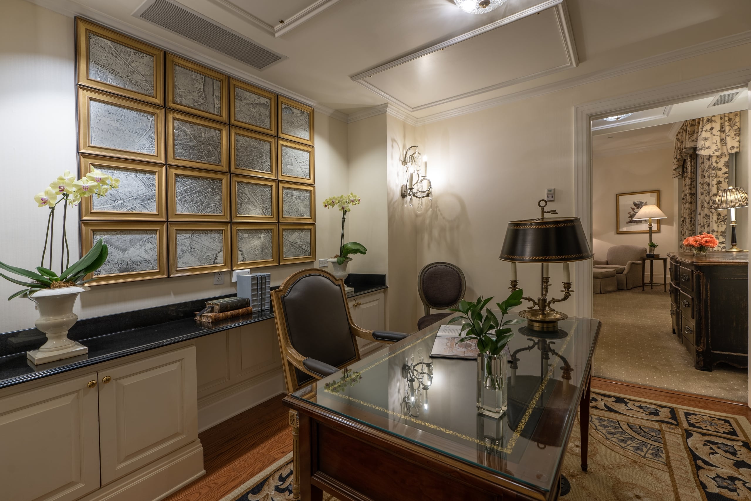Luxurious hotel suite study with a classic desk, ornate lamps, and framed vintage Paris maps.