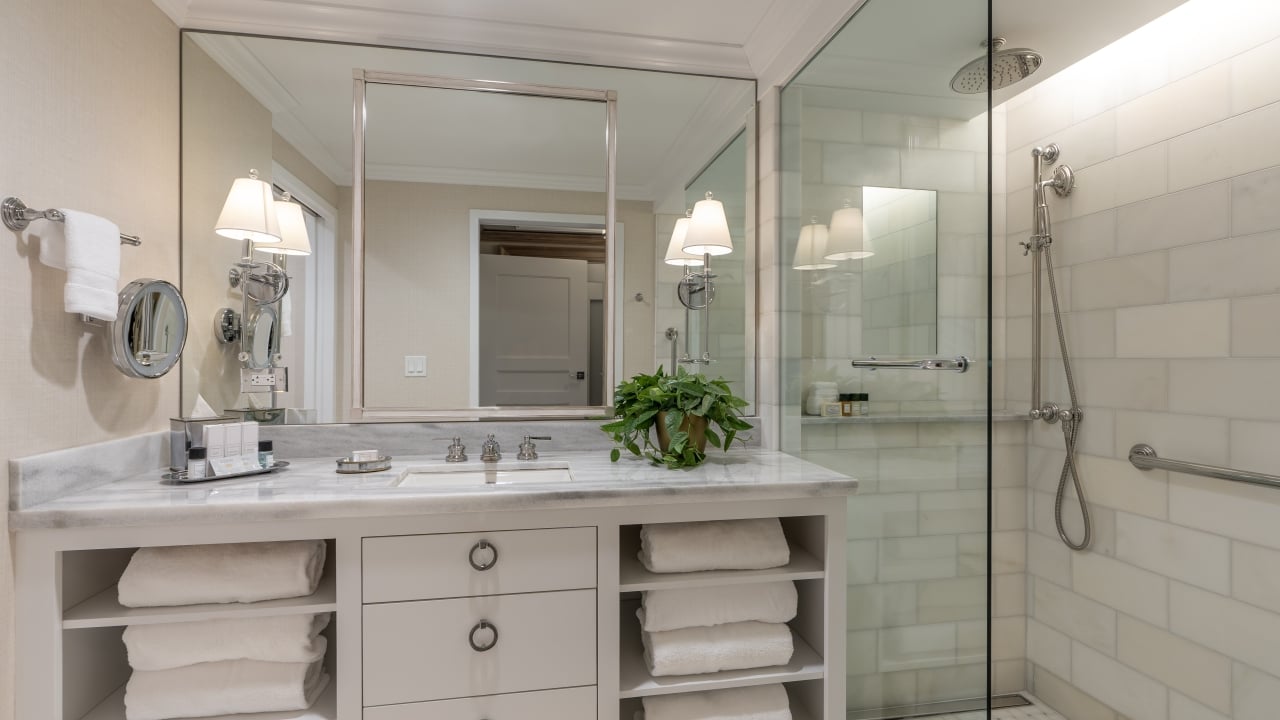 A clean and modern bathroom with a marble countertop, glass-enclosed shower, and a large mirror.