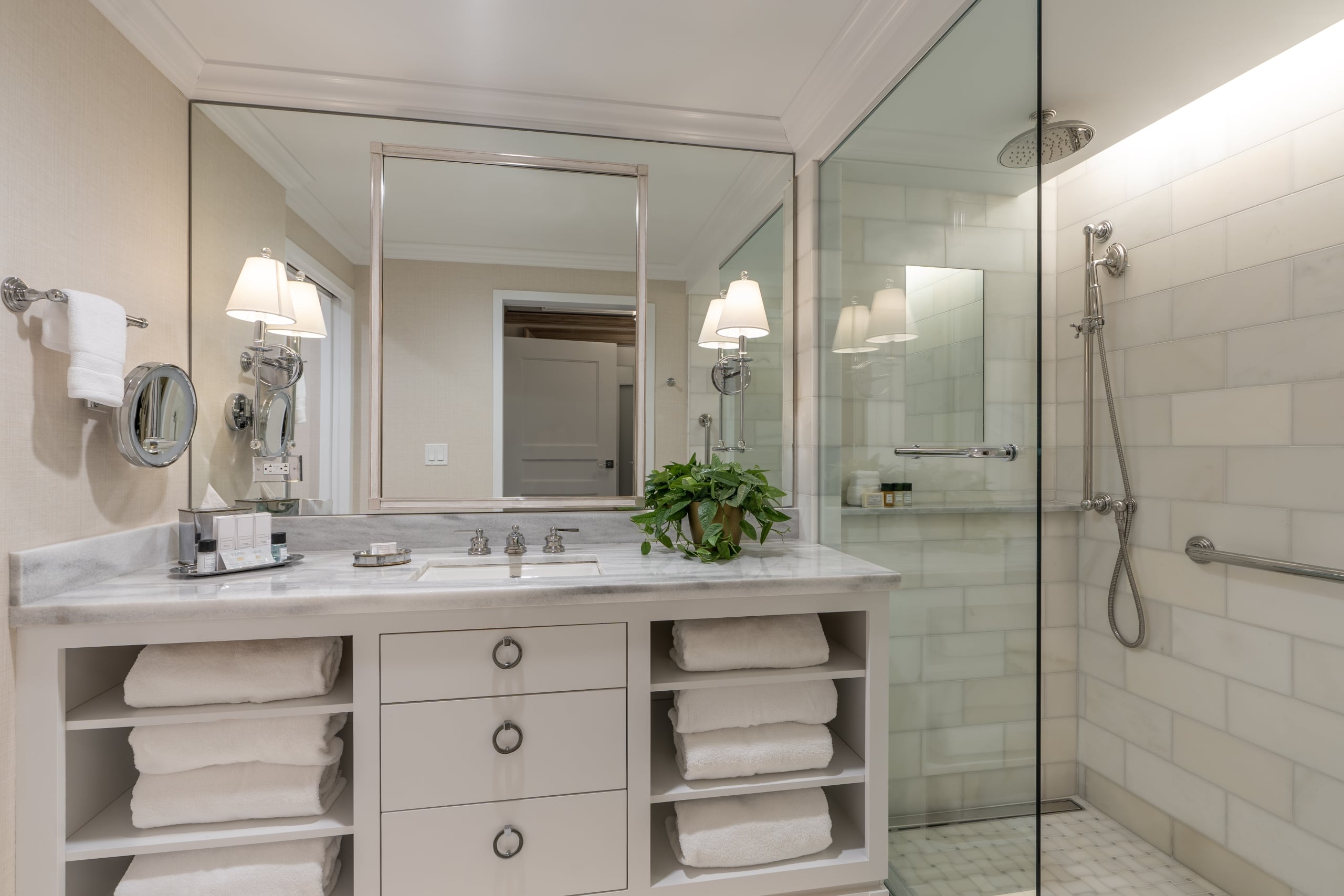 Luxurious New Orleans hotel bathroom featuring marble vanity, large mirror, fresh towels, and a spacious glass shower.