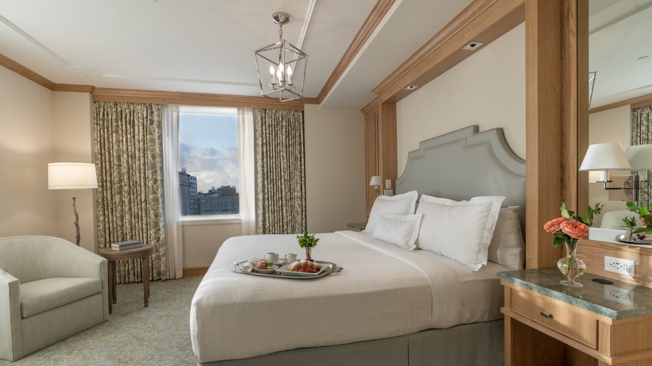 A hotel room with a bed, chair, lamp, and window