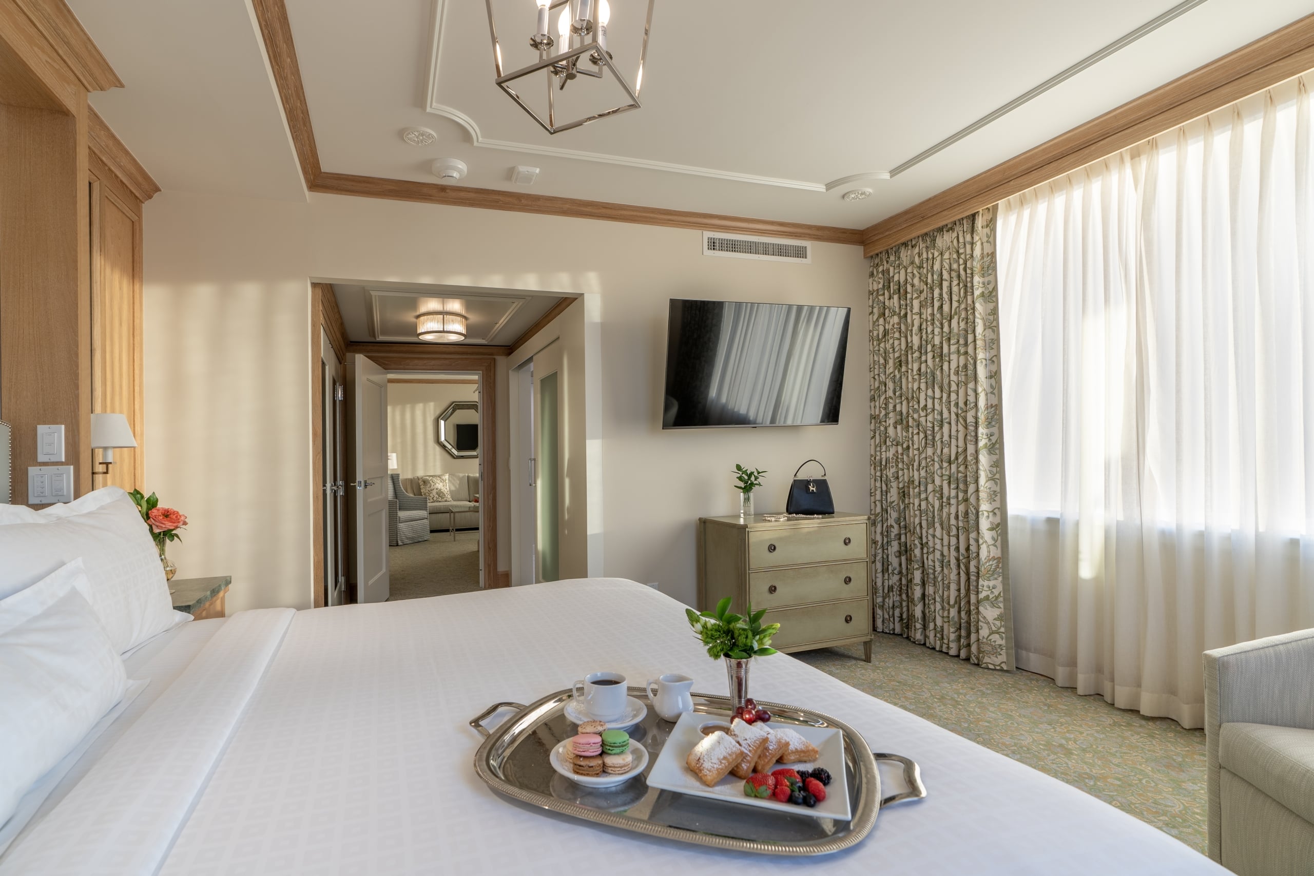 Luxury New Orleans hotel room with breakfast in bed featuring beignets, coffee, and macarons.