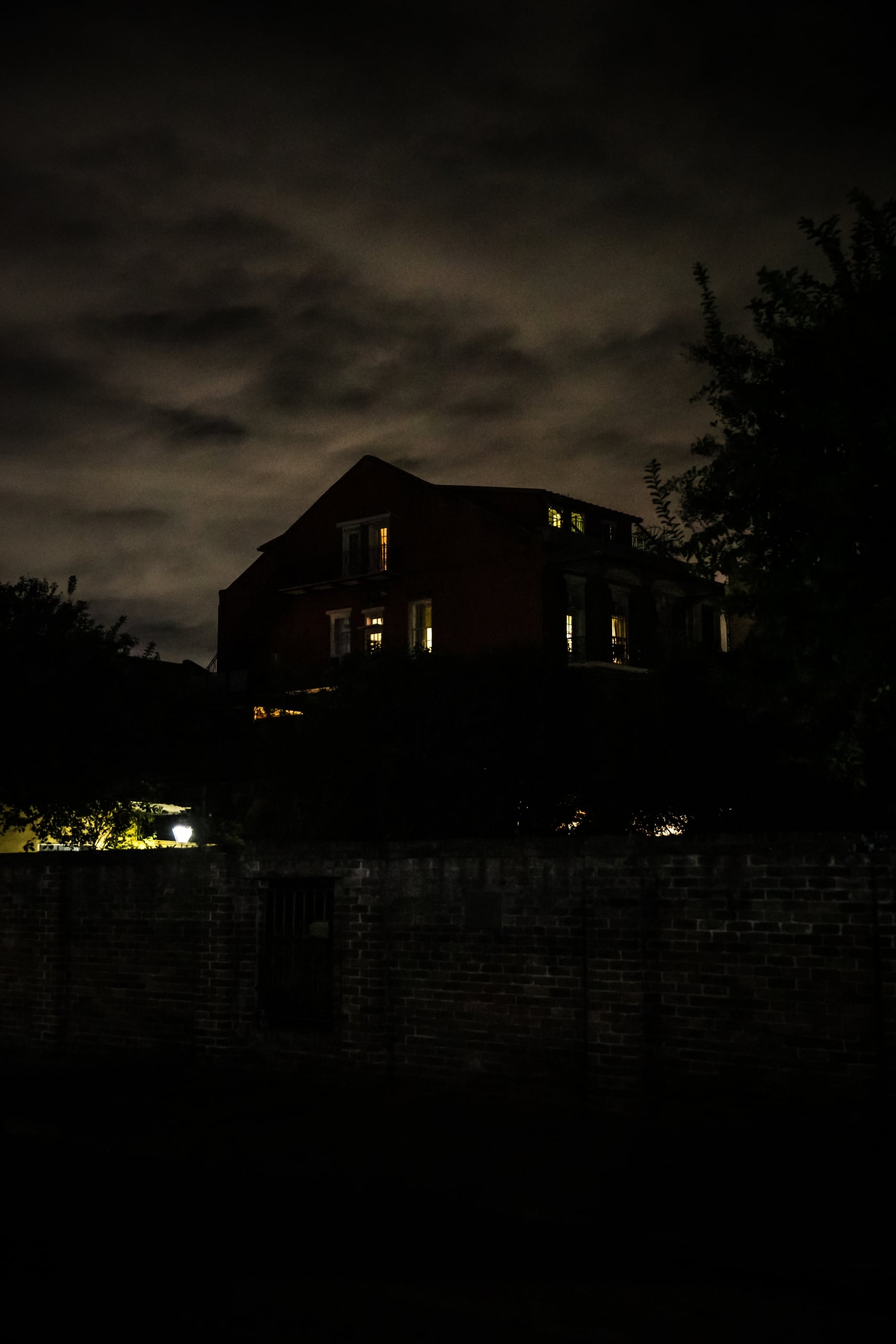 Very dark house and street image with a haunted house looking building in background. Night time, cloudy skies, spooky, creepy.