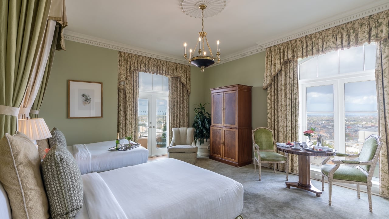 A large hotel room with a bed, desk, chandelier, and window