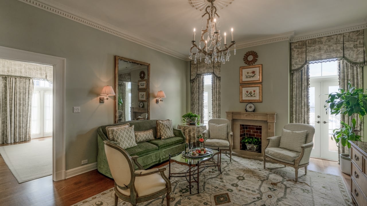 A wide view of a luxurious living room with a green sofa, armchairs, a coffee table, and a fireplace.