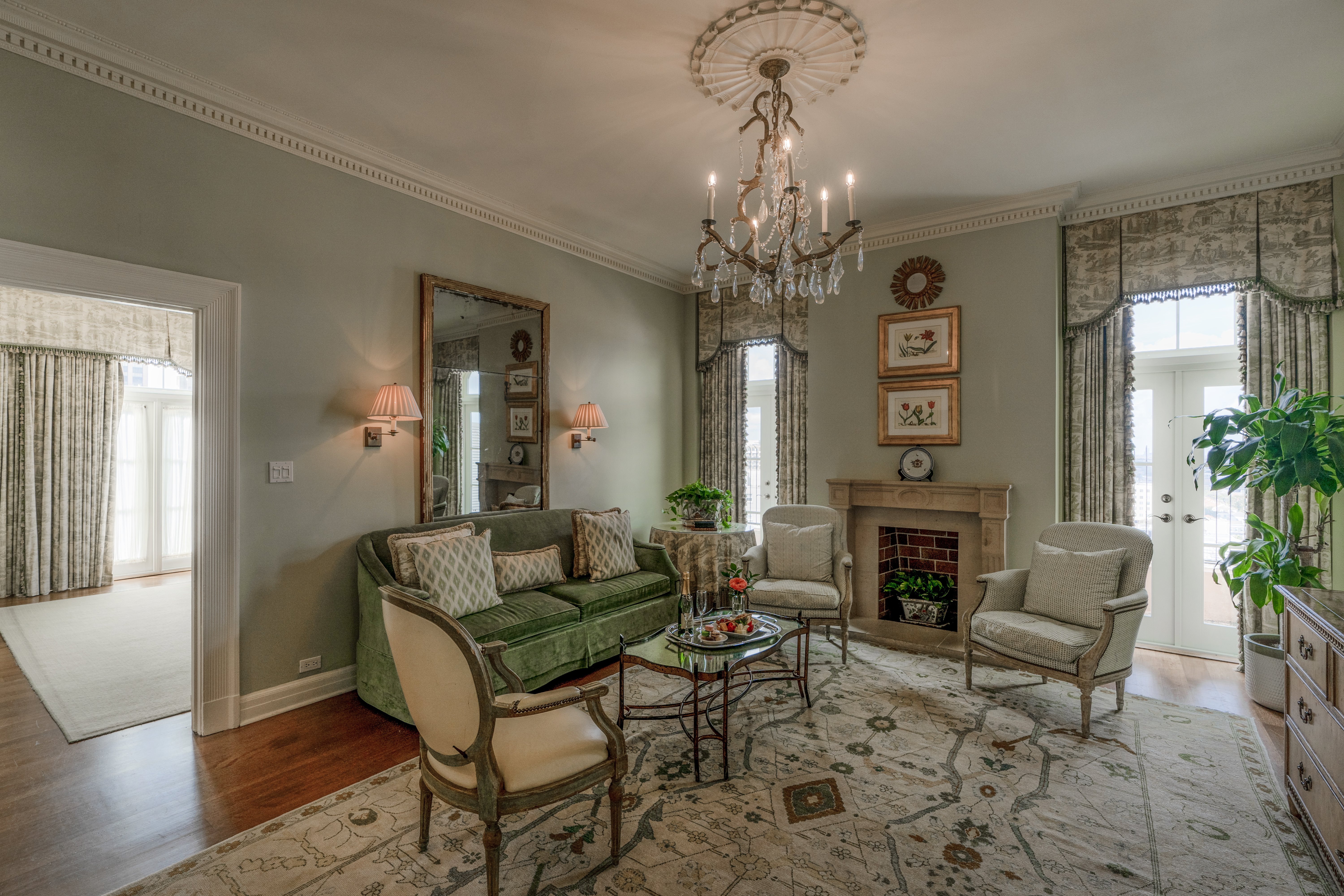 A wide view of a luxurious living room with a green sofa, armchairs, a coffee table, and a fireplace.