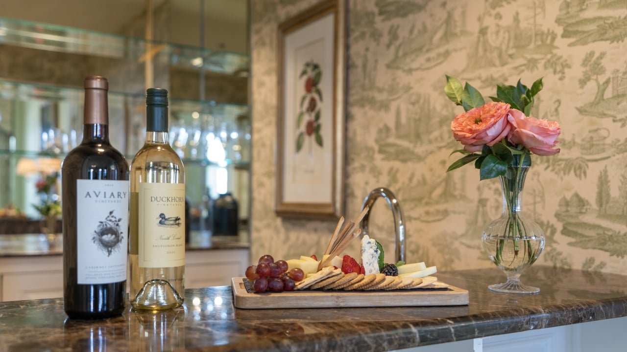 A counter with wine, a cheese board, and flowers