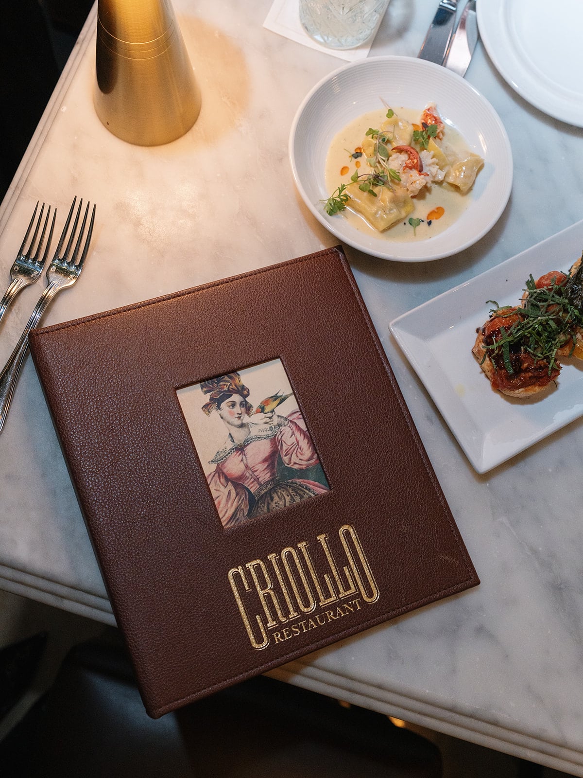 Criollo Restaurant menu, gourmet pasta, and appetizers on a luxurious New Orleans dining table.