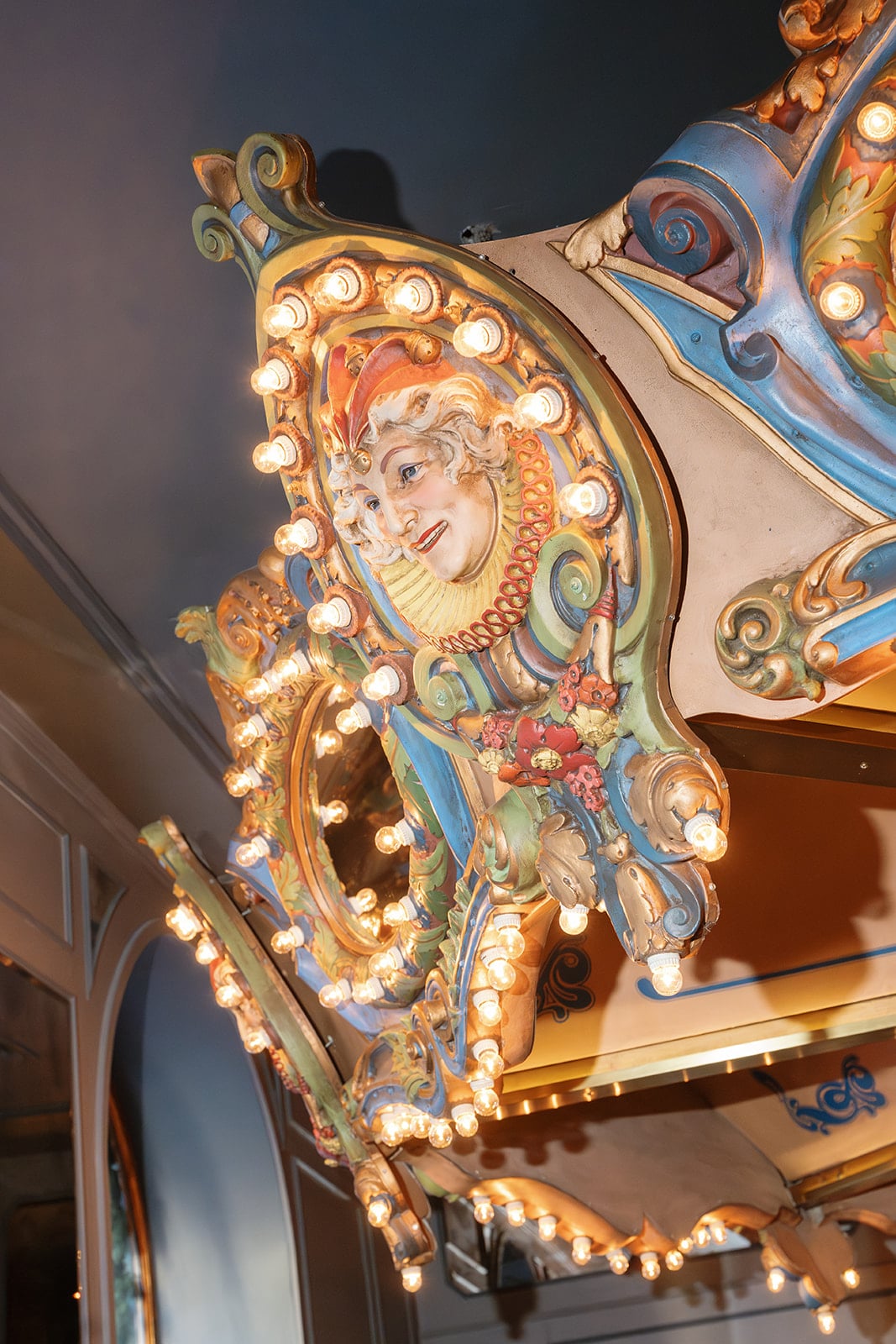 Vintage New Orleans carousel jester face with ornate carvings and glowing lights.
