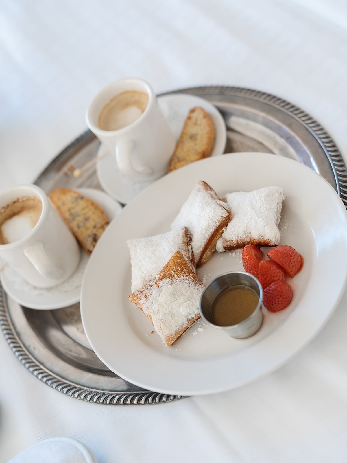 Fresh New Orleans beignets with powdered sugar, coffee, and strawberries on a silver room service tray.