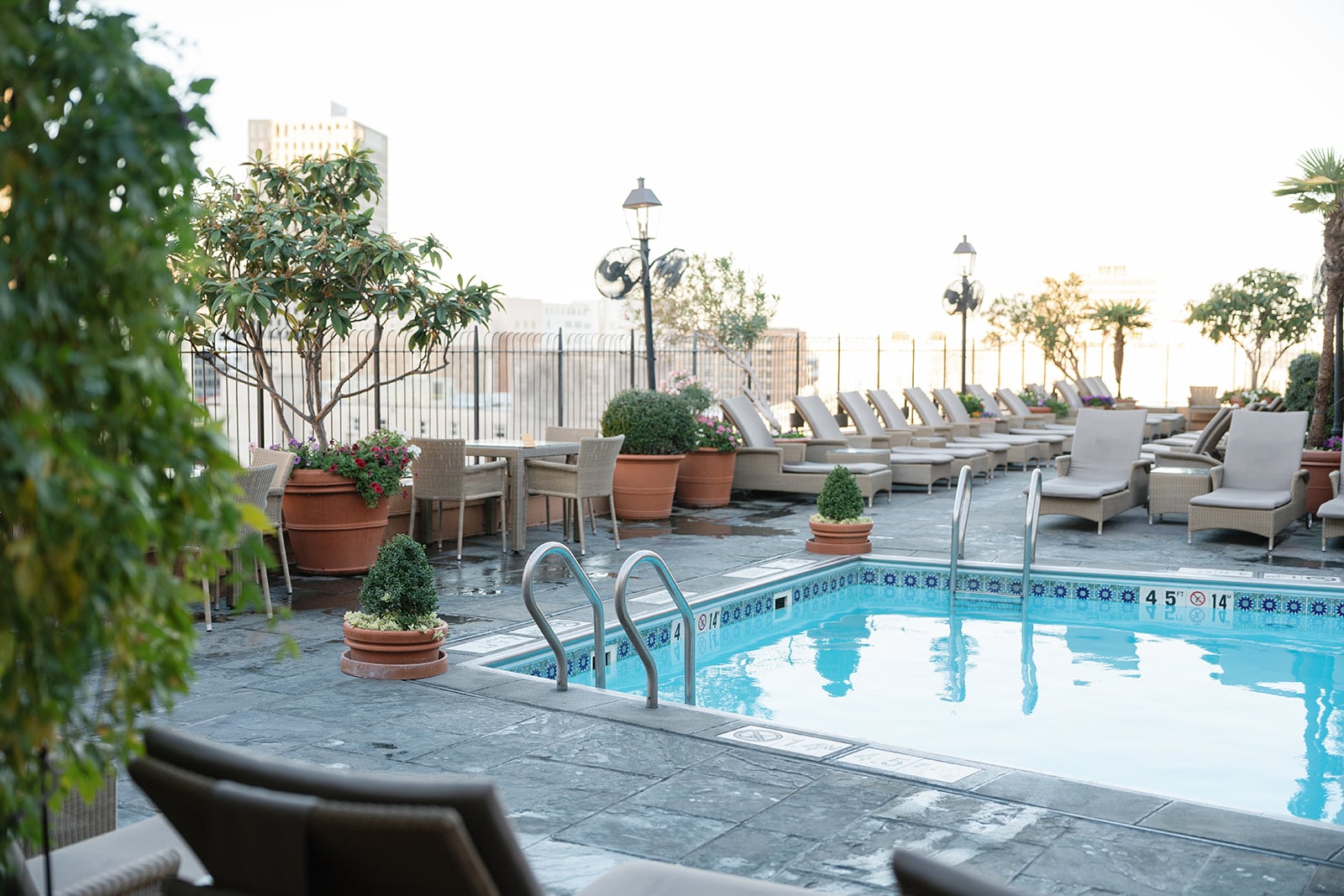 New Orleans rooftop pool with lounge chairs, dining tables, and lush potted plants.