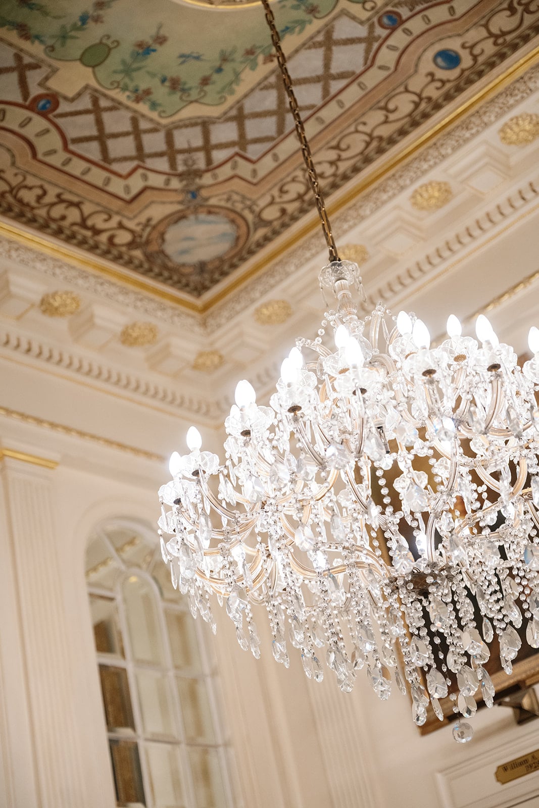 Ornate crystal chandelier and gilded, hand-painted ceiling in a luxury New Orleans hotel.
