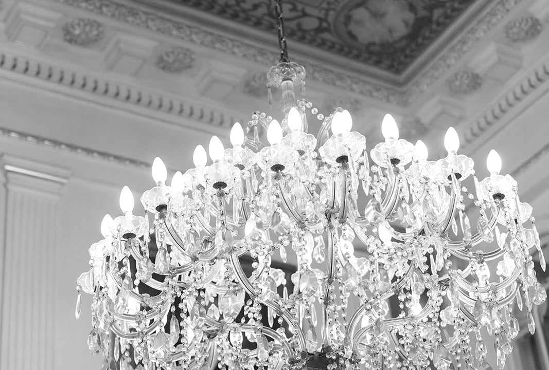 A large, ornate chandelier hangs from a ceiling with intricate molding.