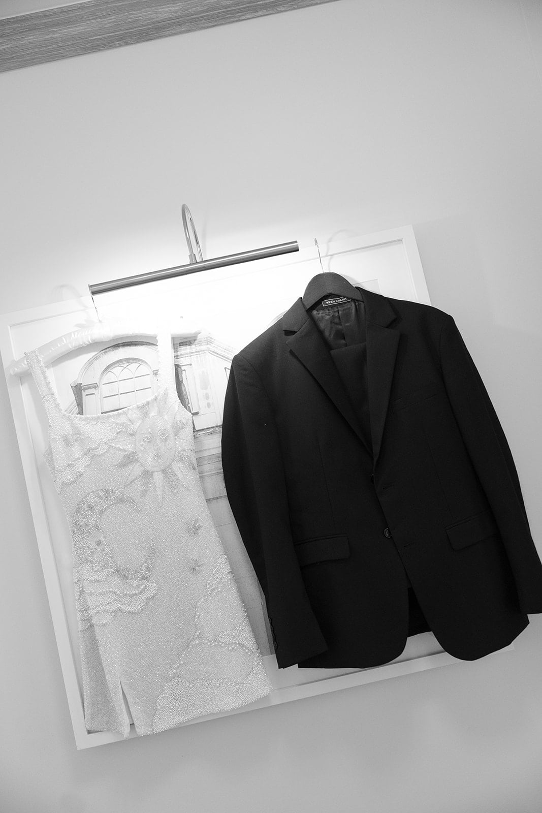 Ornate white dress and black suit jacket hanging, ready for a New Orleans celebration.