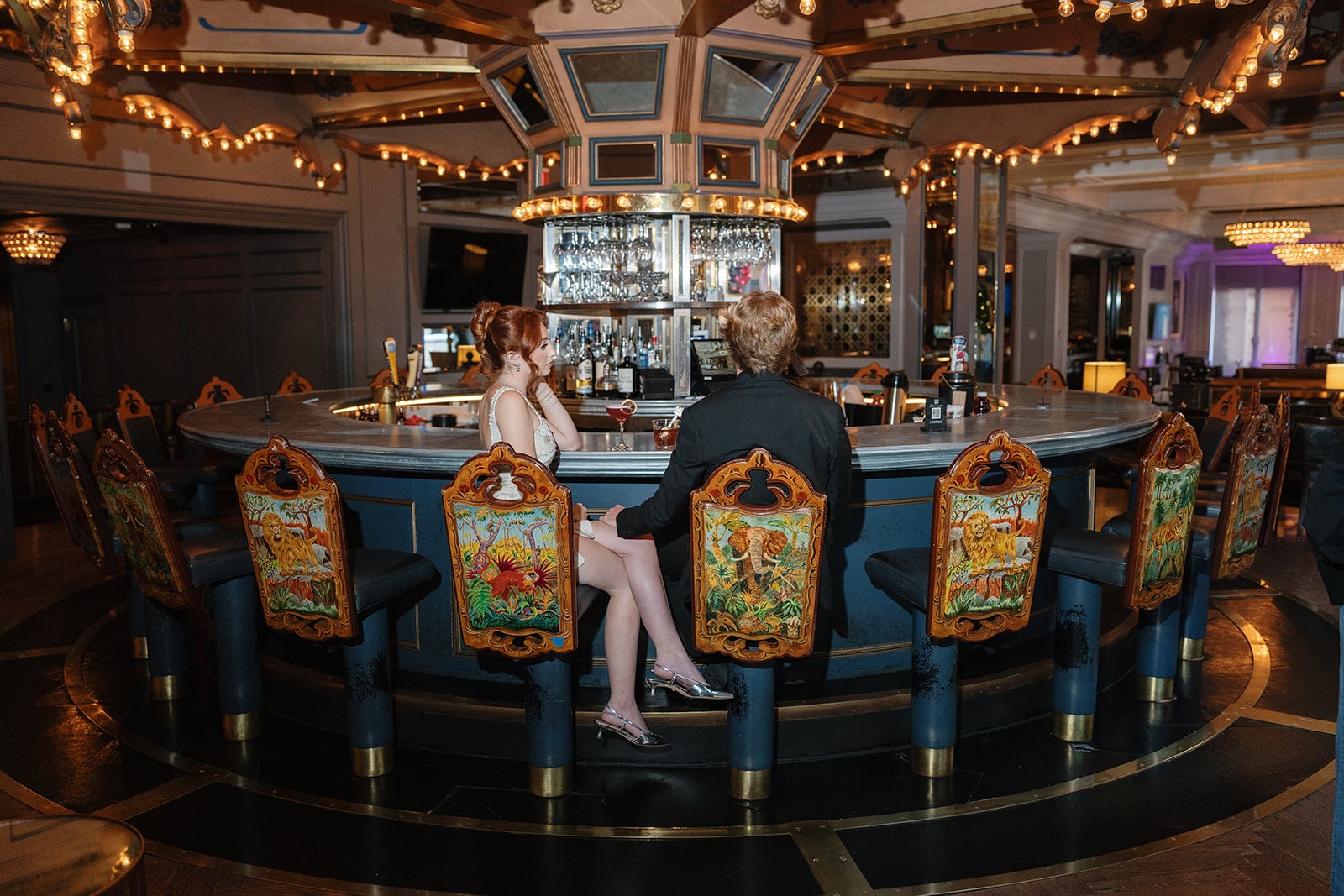 Guests at a luxurious New Orleans bar with unique animal-themed chairs and a lit, carousel-inspired ceiling.
