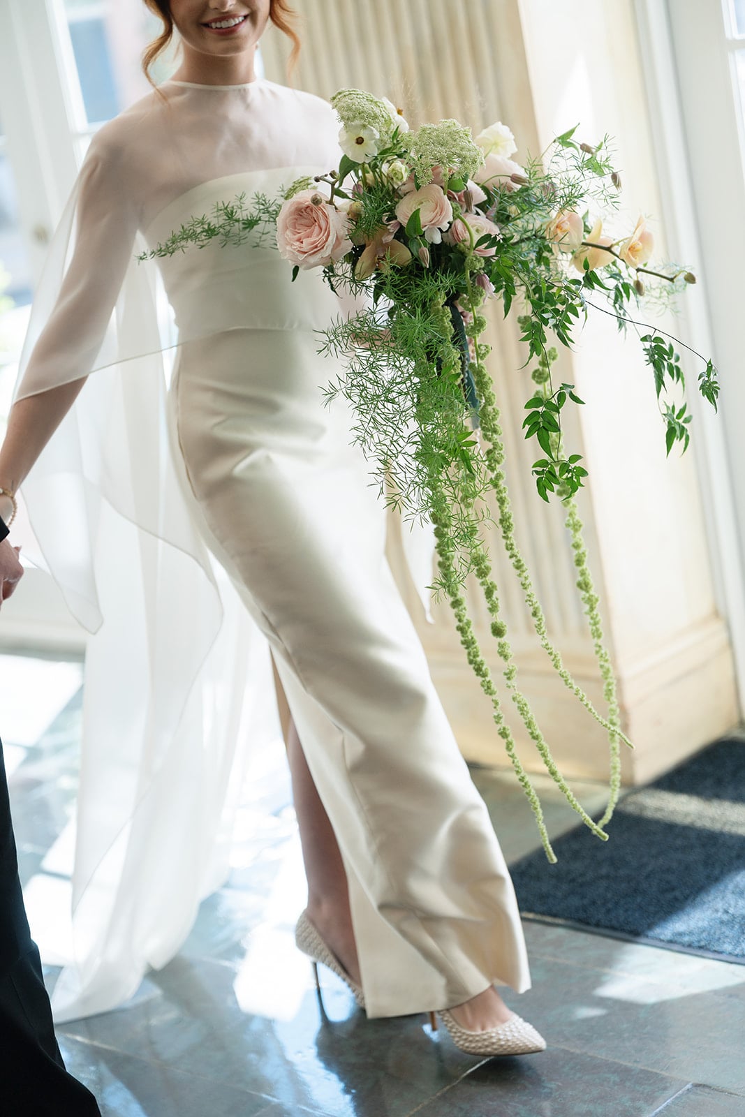 Detail shot of a bride walking indoors, highlighting her pearl-studded heels and a lush, trailing floral bouquet.